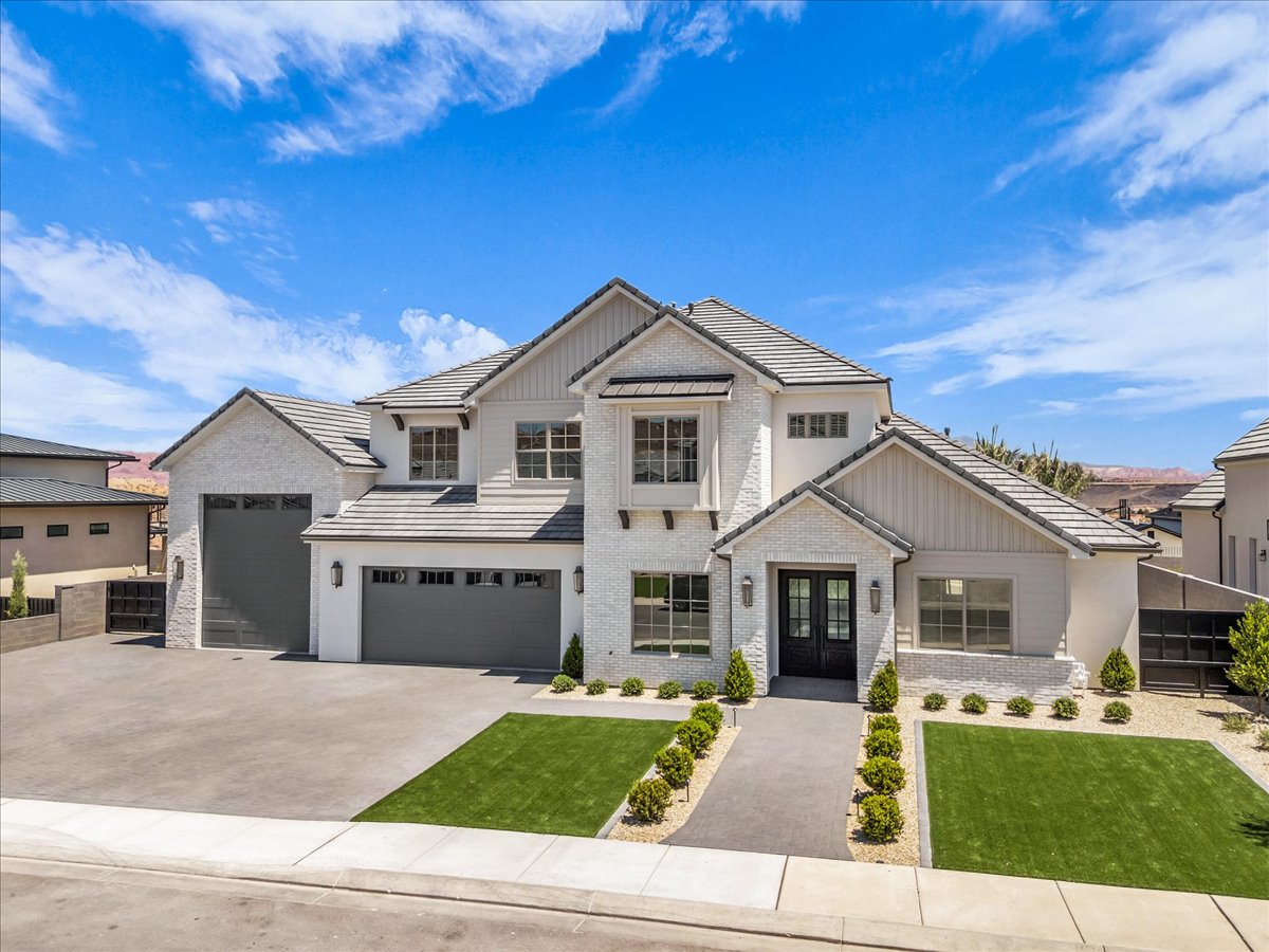 Contemporary residence featuring a light-colored brick and stucco exterior, dark composite roof shingles, multiple dark garage doors, a double front entry door, and a concrete driveway