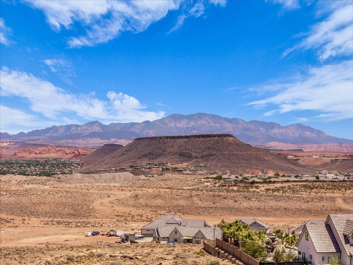 Expansive desert landscape featuring distant mountains, red rock formations, and a clear blue sky