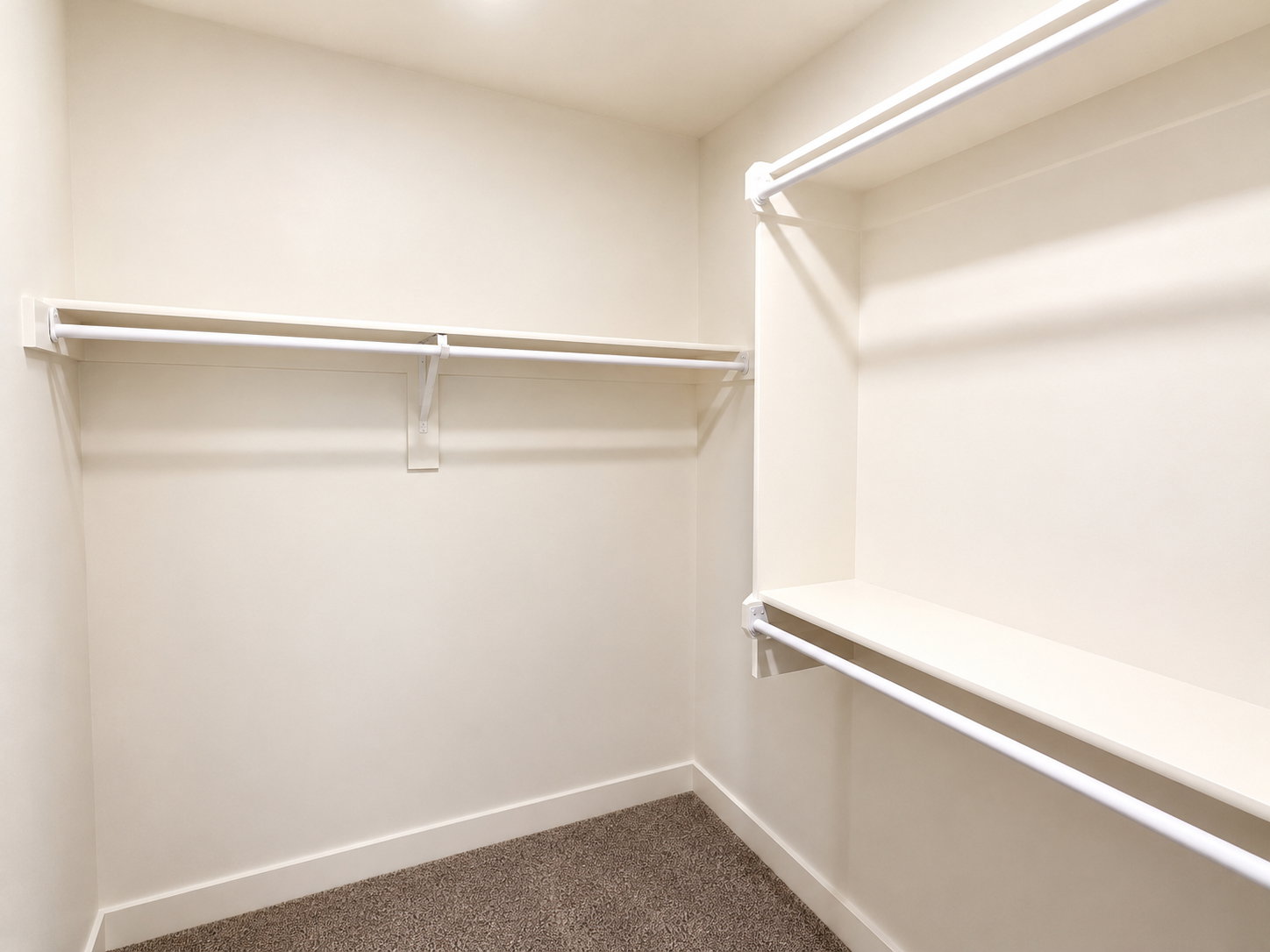 Walk-in closet with neutral-toned walls, white shelving, and hanging rods