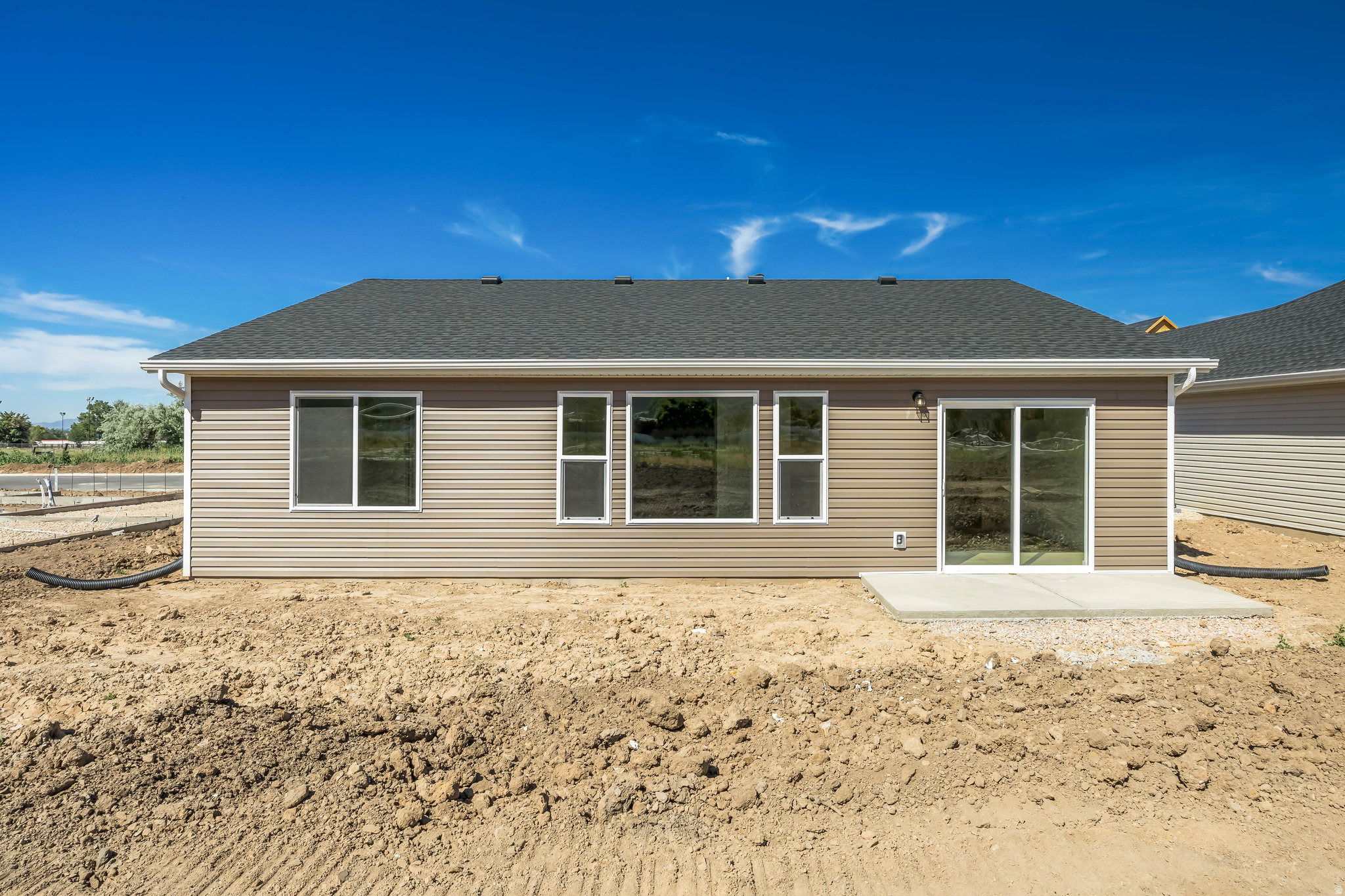 Rear exterior of a single-story residence featuring tan horizontal siding, a dark shingle roof, and white rain gutters