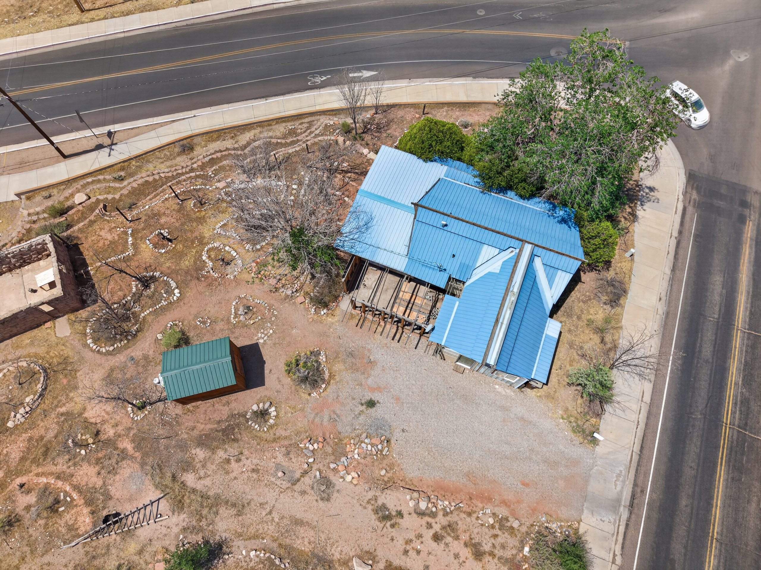 Property featuring a bright blue metal roof, an additional green metal-roofed structure, and a large shade tree