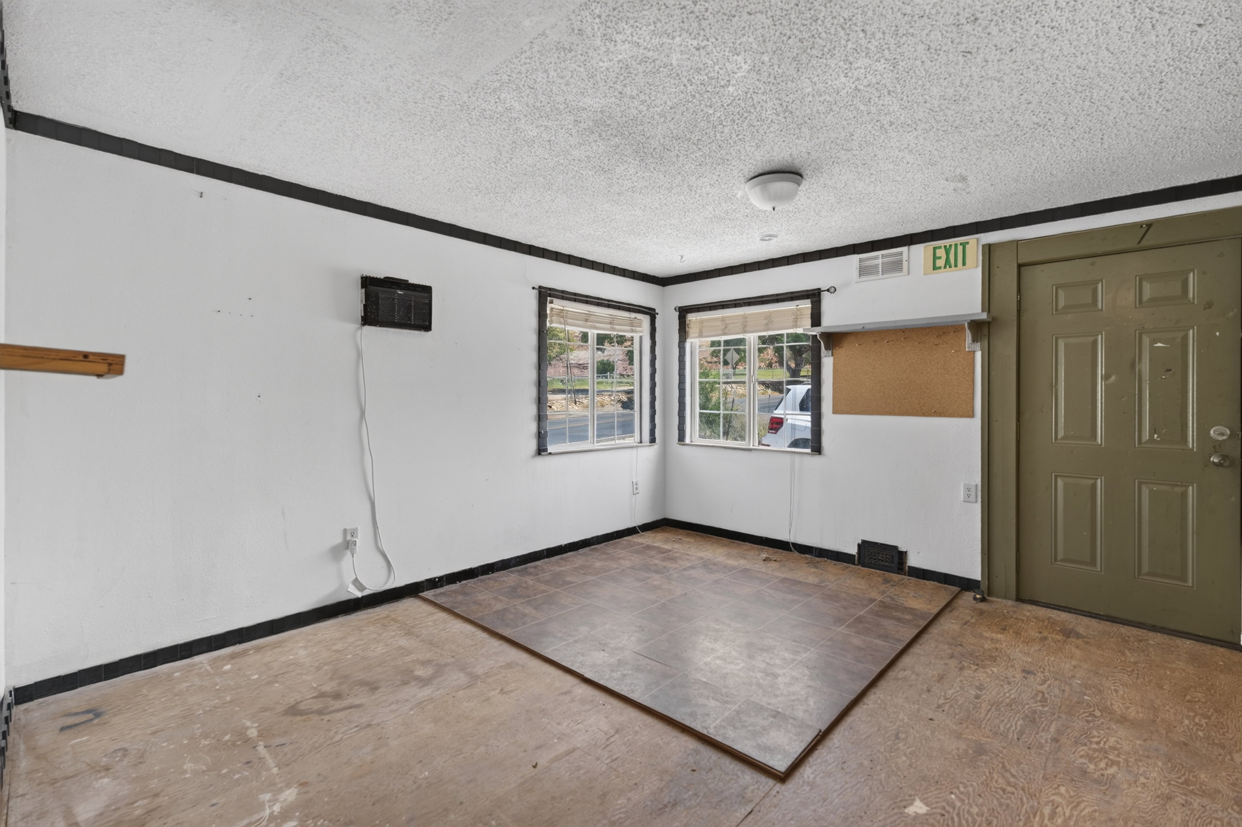 Versatile interior space featuring two windows with horizontal blinds, a paneled door, and a textured ceiling