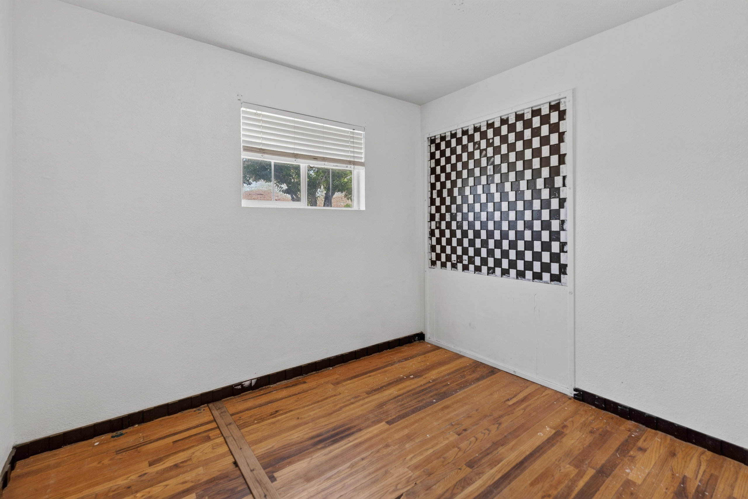 Room featuring wood-finish flooring, white walls, and a window with blinds