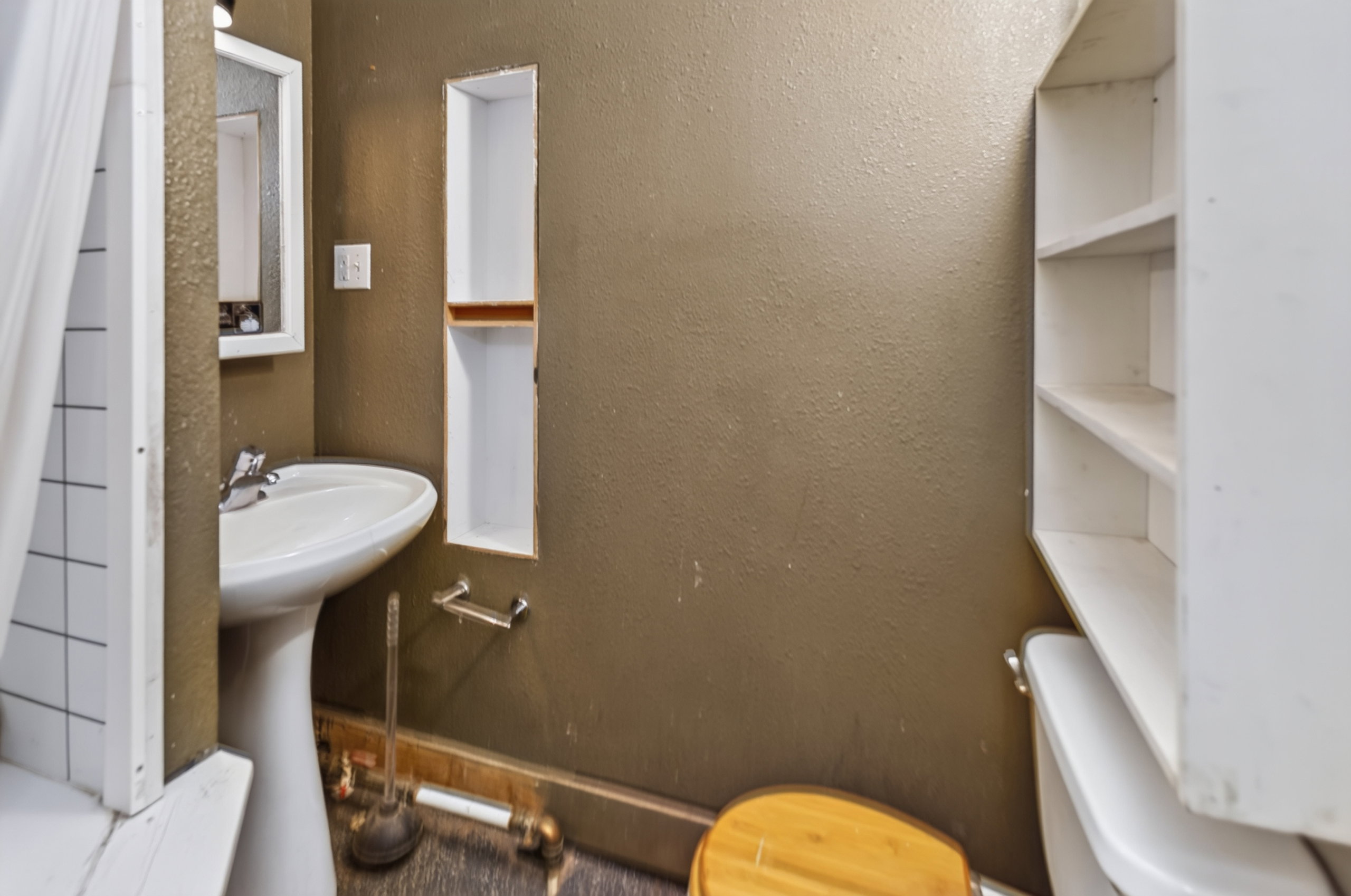 Pedestal sink with chrome faucet, framed wall mirror, and built-in wall niche with wood-finish shelf