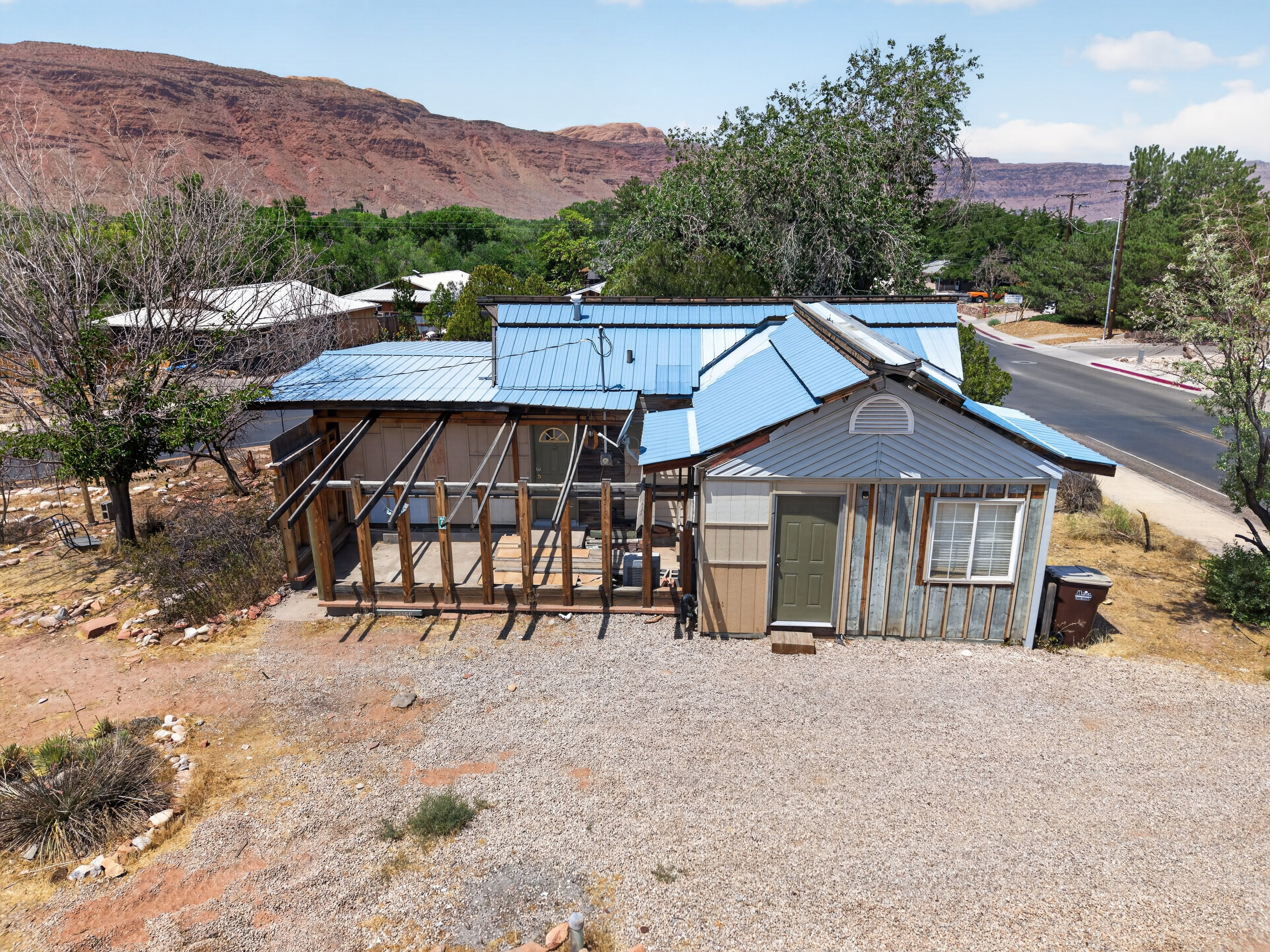 Property featuring a light blue metal roof, an angled porch structure, and a gravel driveway