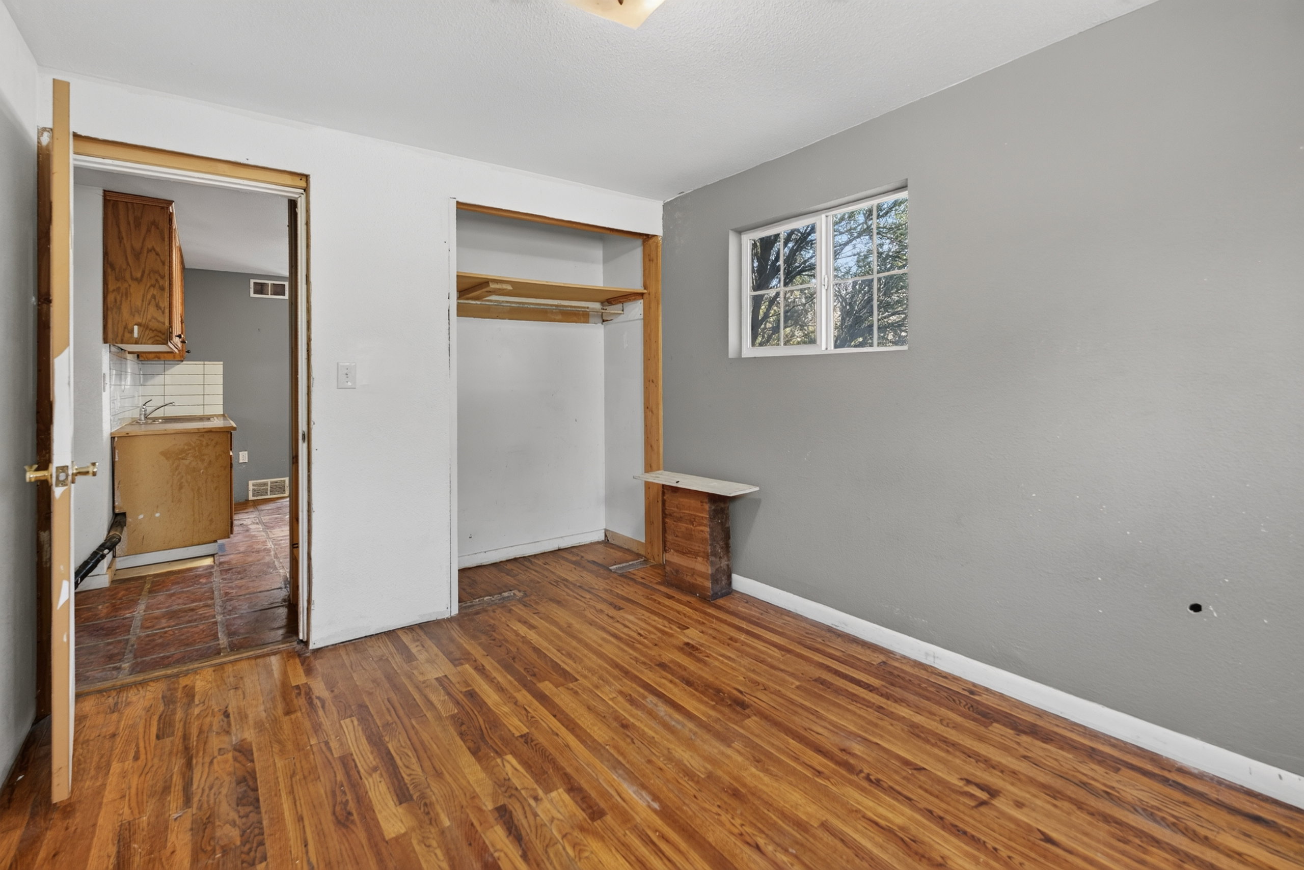 Room featuring wood-finish flooring, a double-hung window, and an open closet with shelving and hanging rod