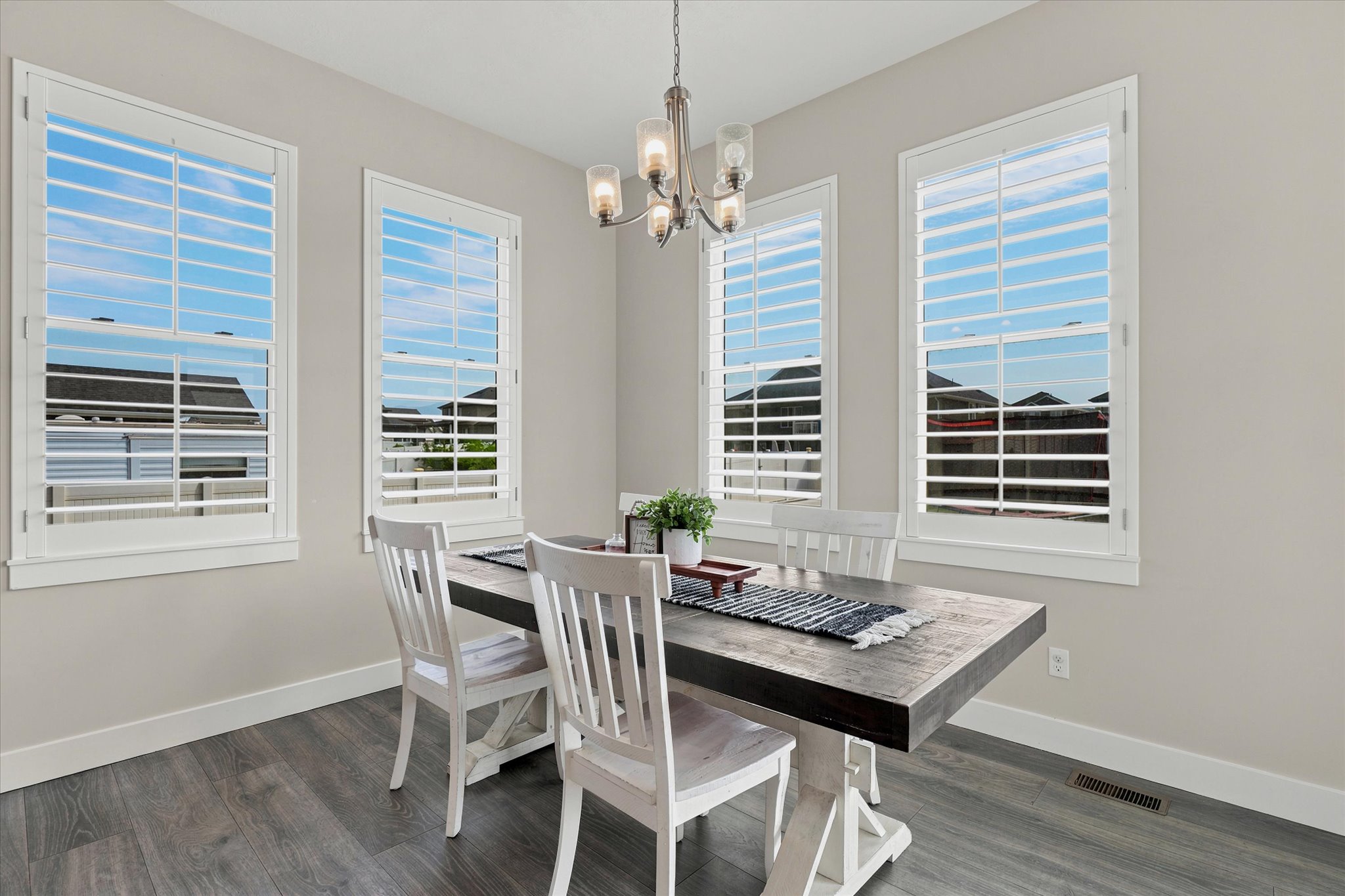 Dining area with four windows featuring white plantation shutters, wood-finish flooring, and a chandelier with glass shades