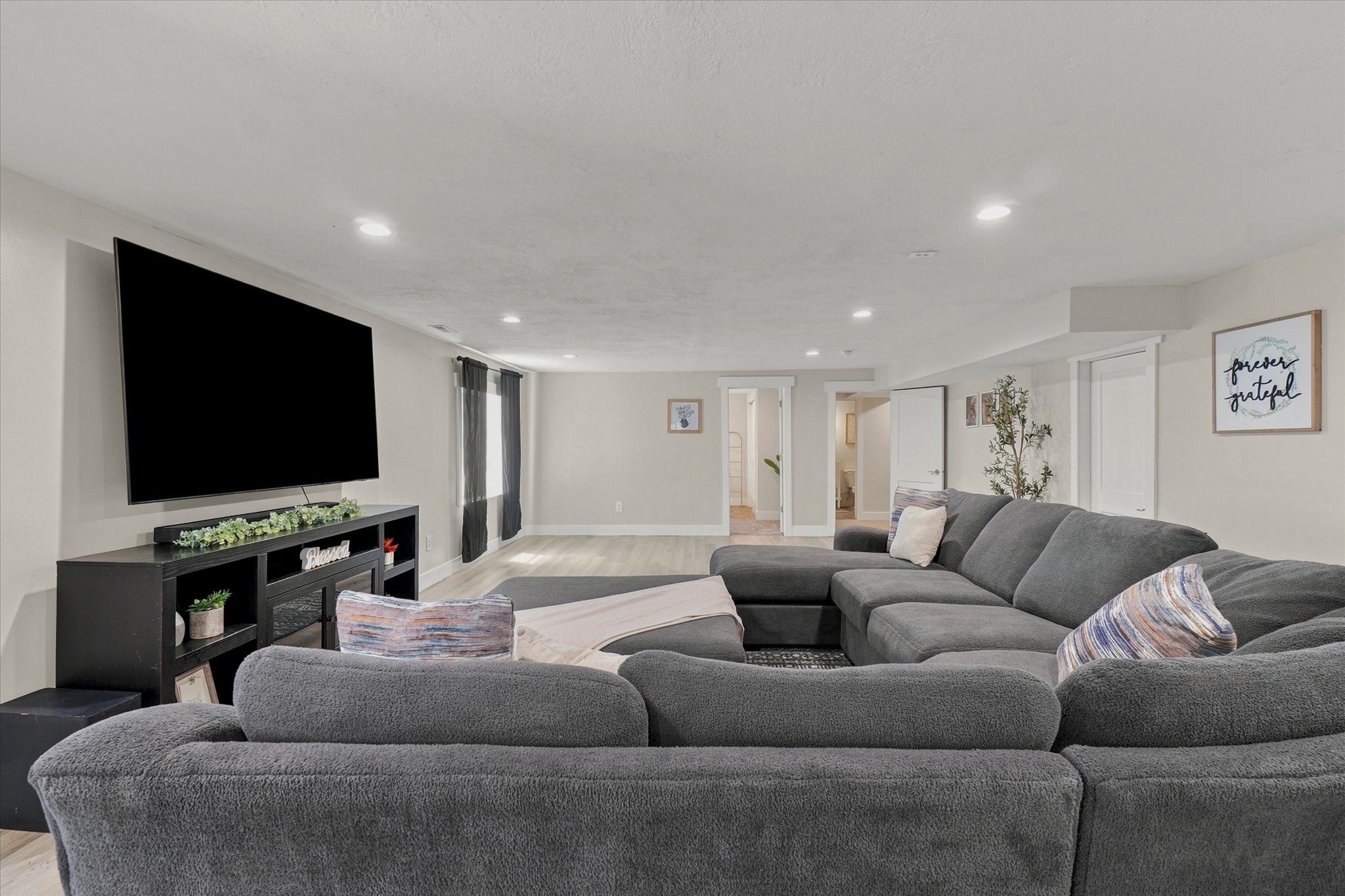 Spacious living area featuring light-toned walls, recessed lighting, wood-finish flooring, and white trim