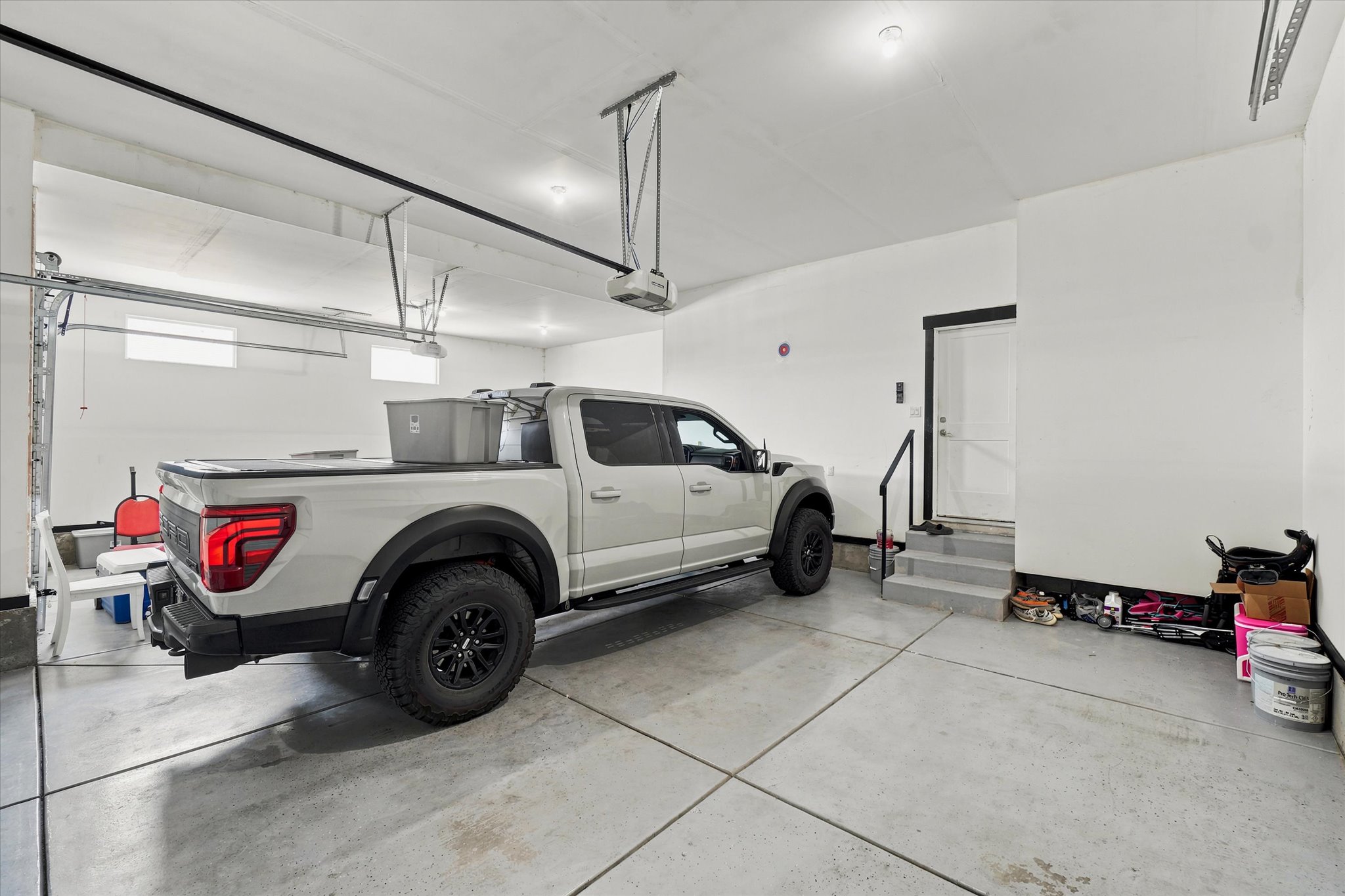 Attached garage featuring a concrete floor, white walls, and overhead lighting