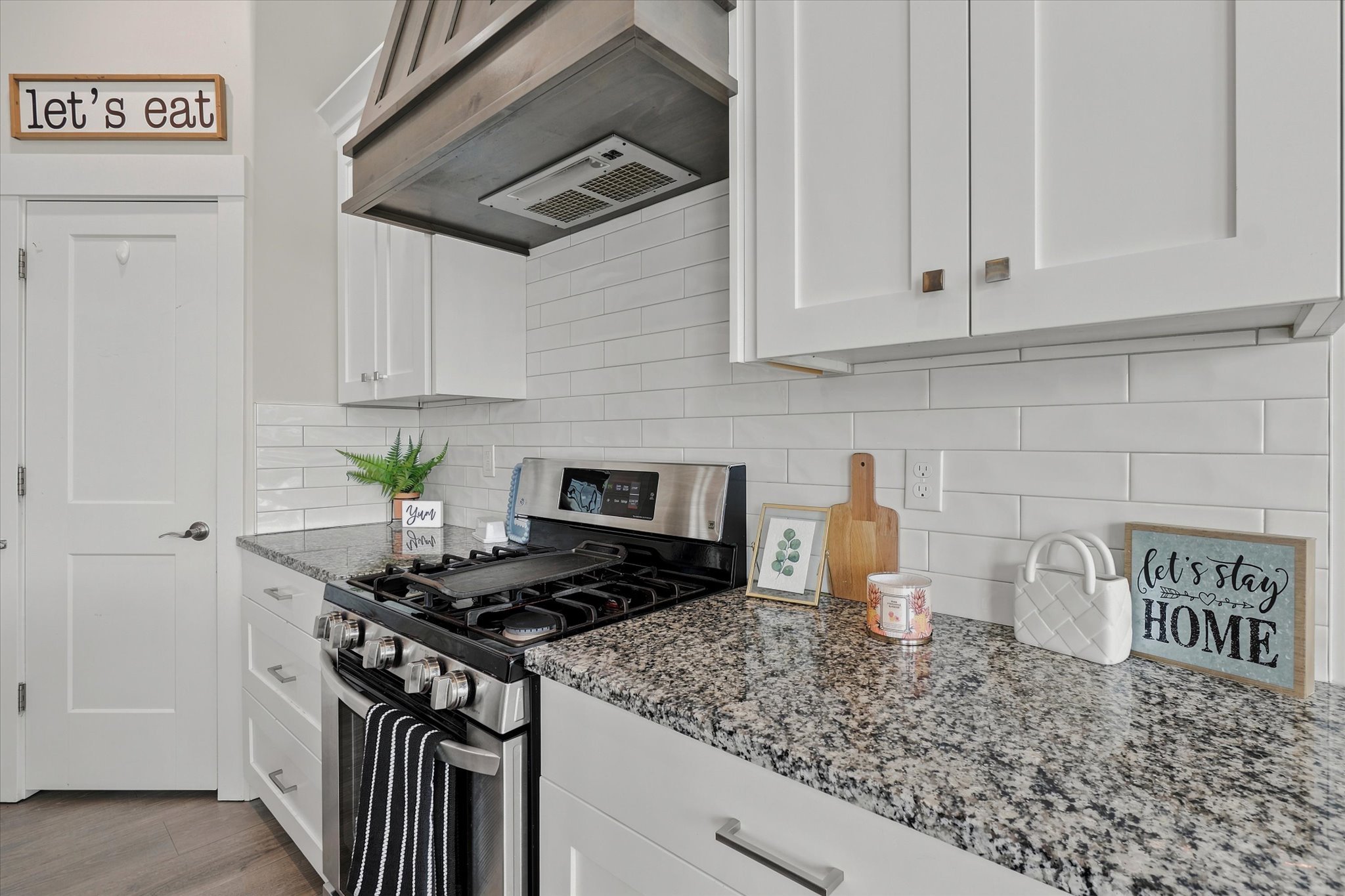 Modern kitchen featuring white shaker cabinetry, speckled countertop, subway tile backsplash, stainless steel range, and a wood-finish range hood