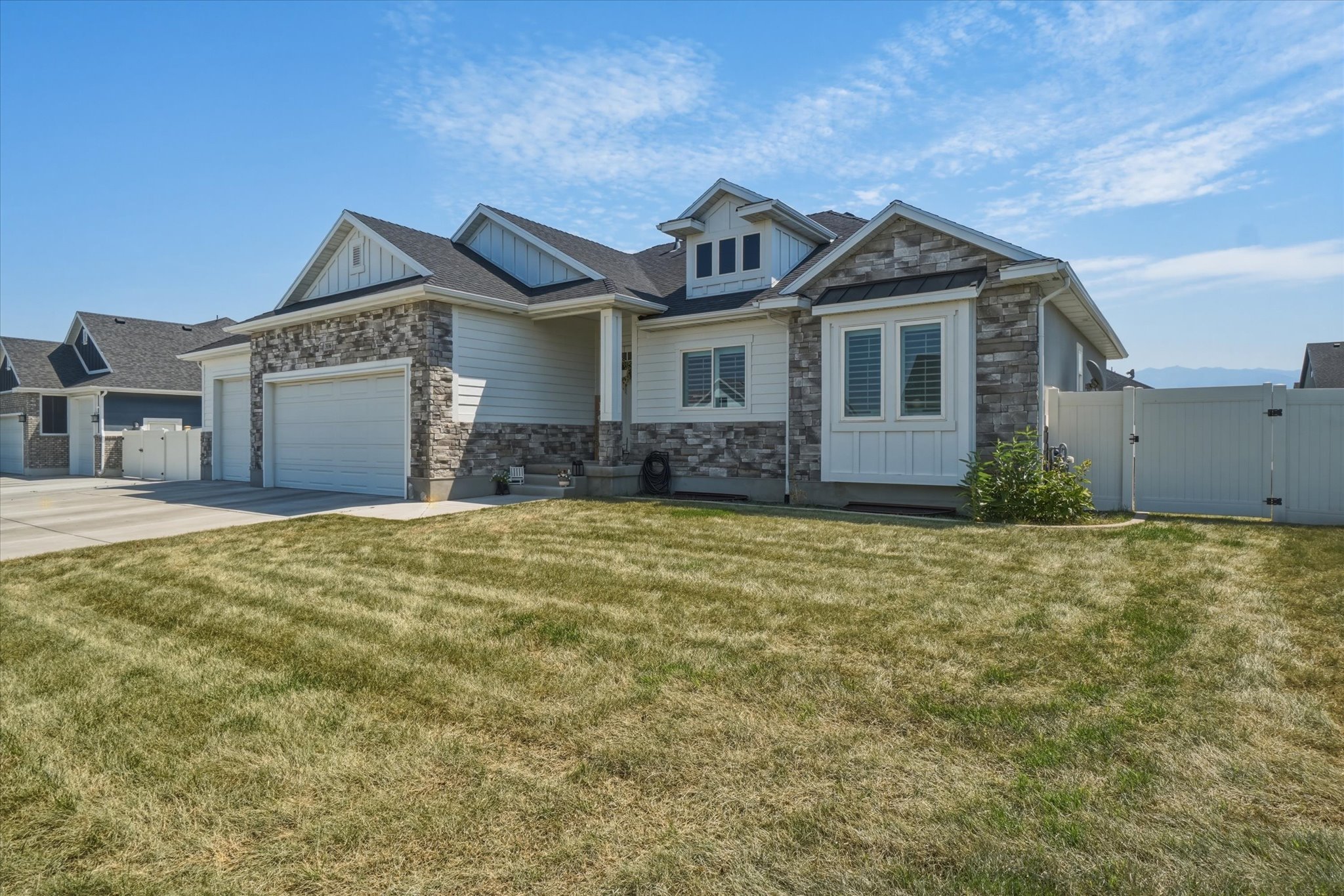 Modern home exterior with stacked stone accents, horizontal siding, a two-car garage, and a white privacy fence