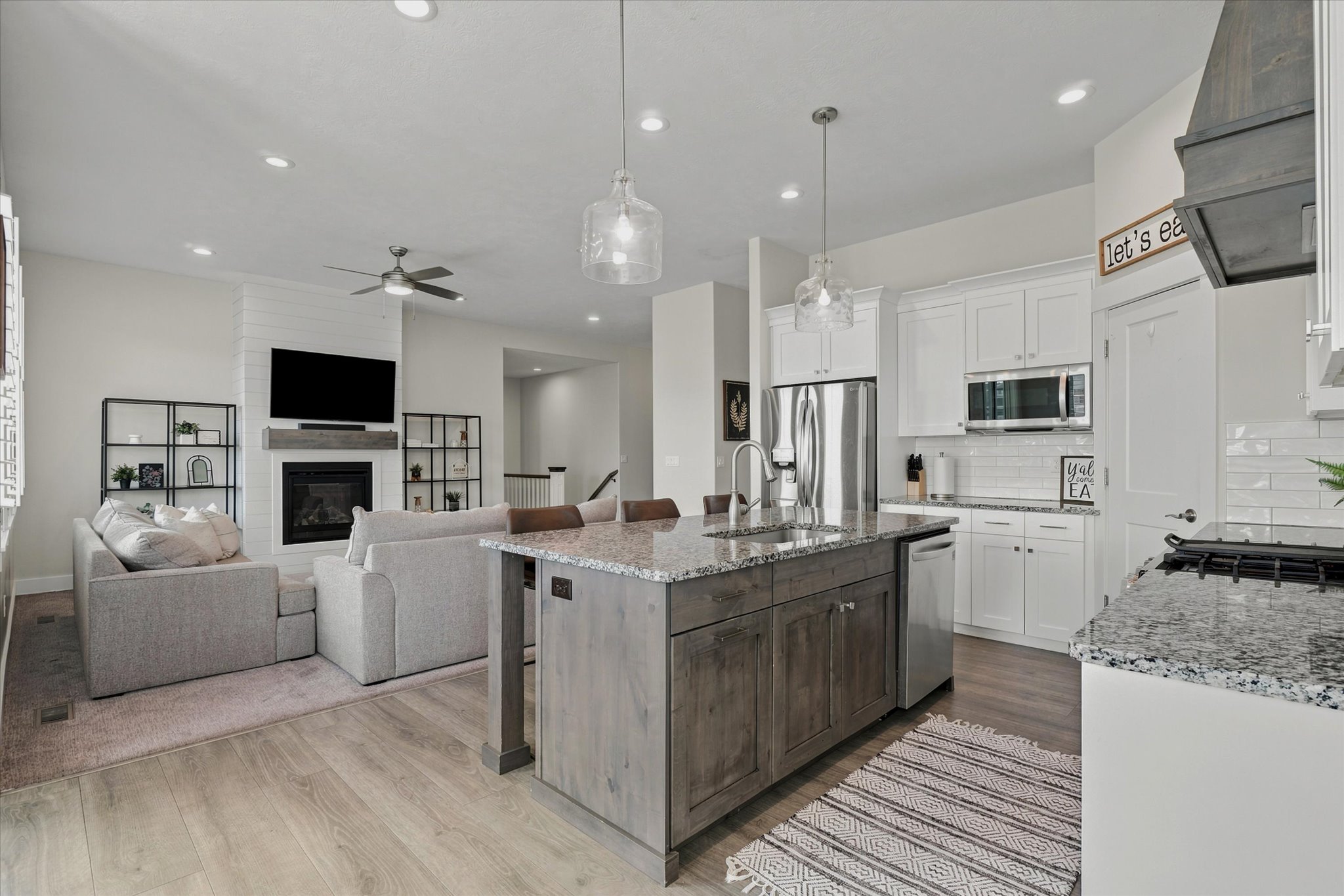 Open-concept living space featuring a kitchen island with seating, pendant lighting, stainless steel appliances, and wood-finish flooring