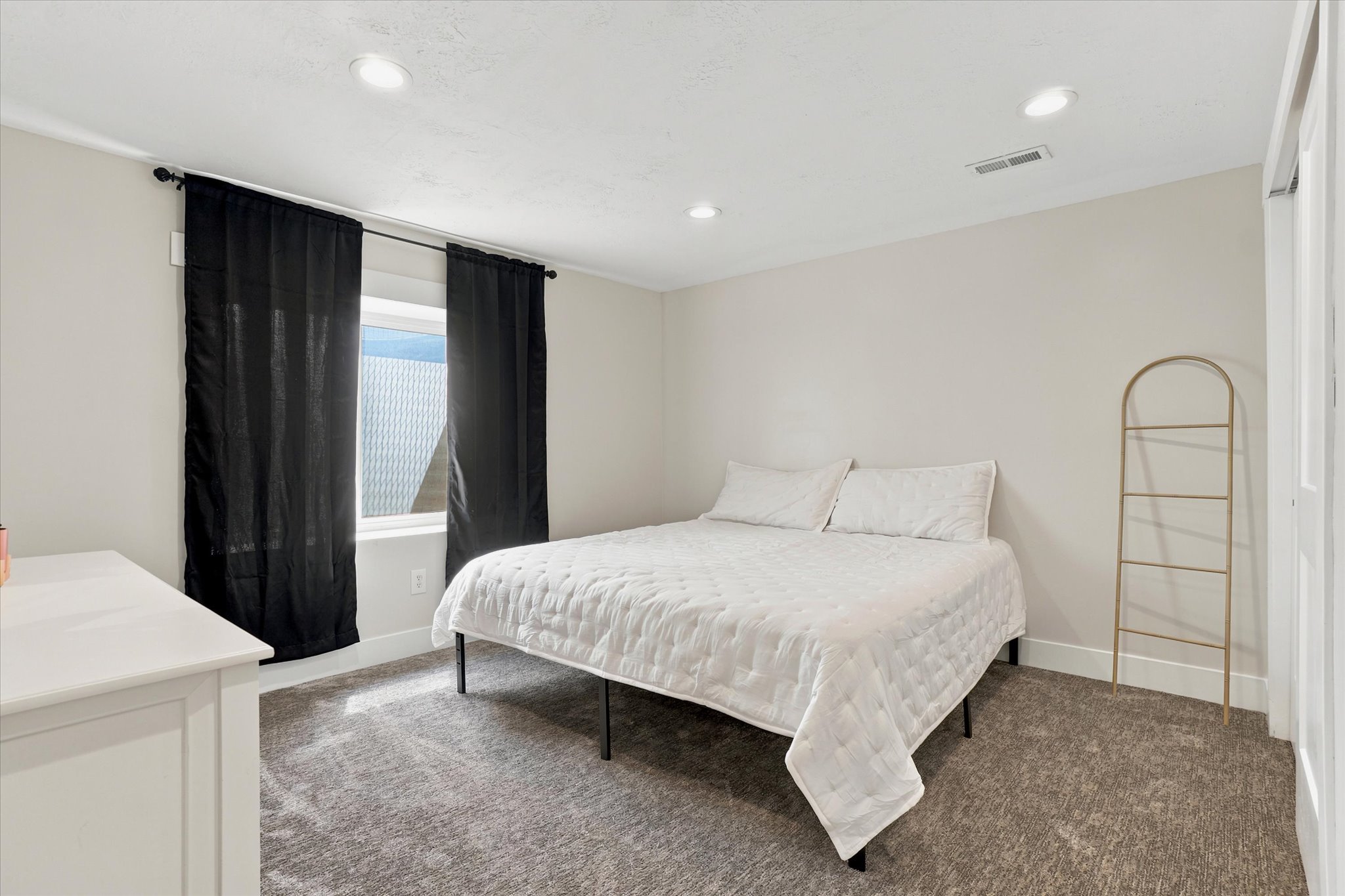 Carpeted room featuring a window with black curtains, recessed lighting, and a white dresser