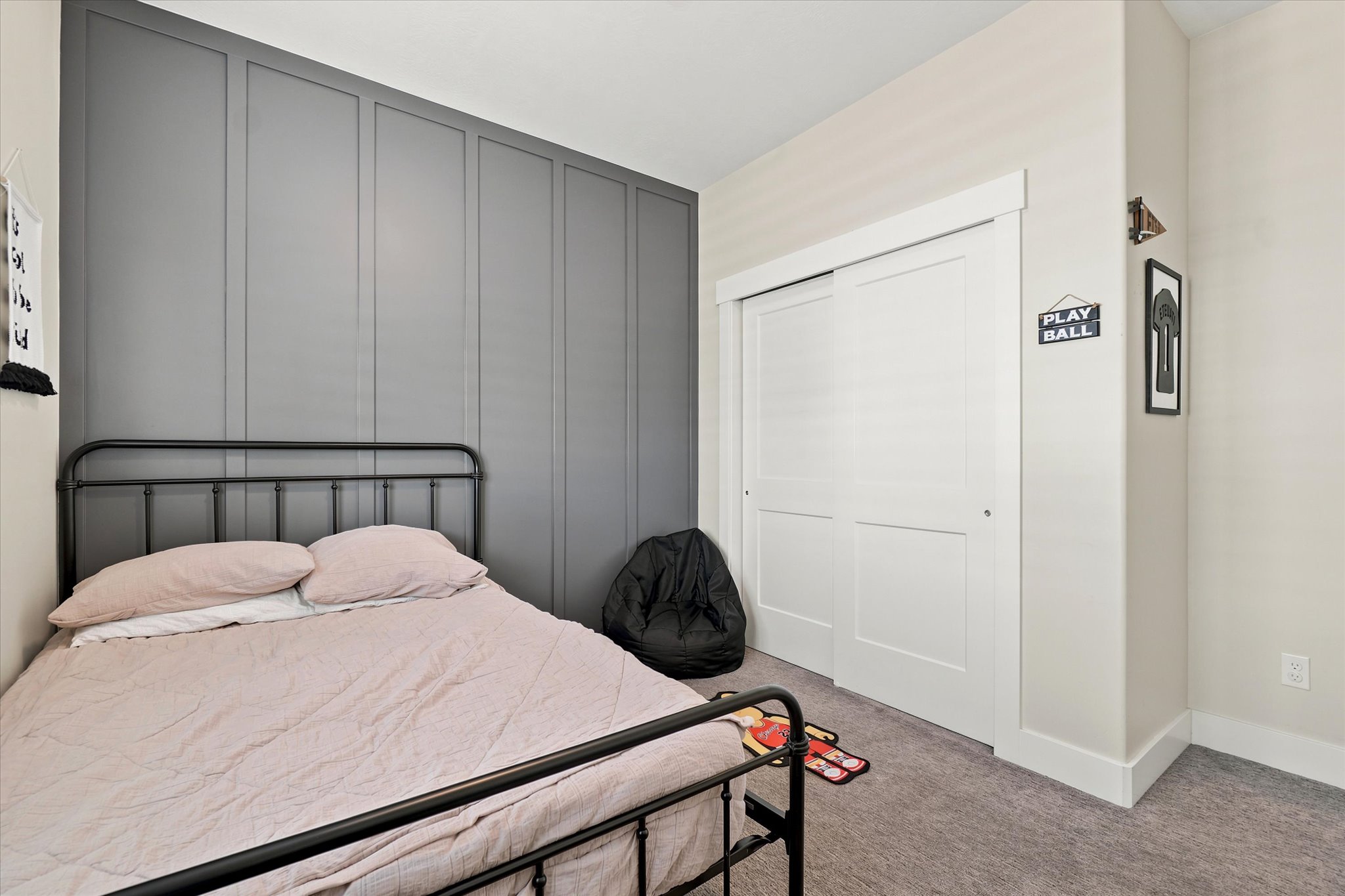 Bedroom featuring a gray accent wall with vertical paneling, light neutral wall paint, white trim, and gray carpeting