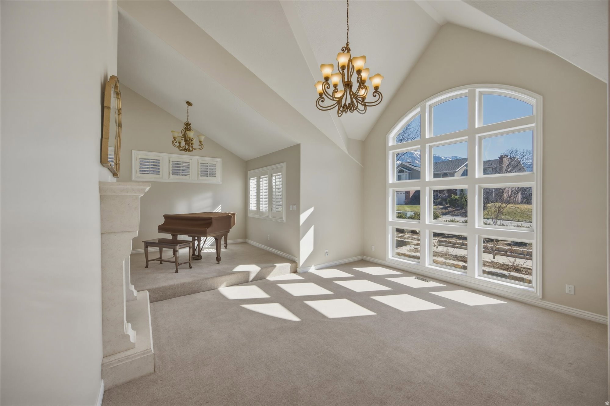 Vaulted ceiling room featuring a large arched window with grid details, a stone fireplace, and a tiered architectural element