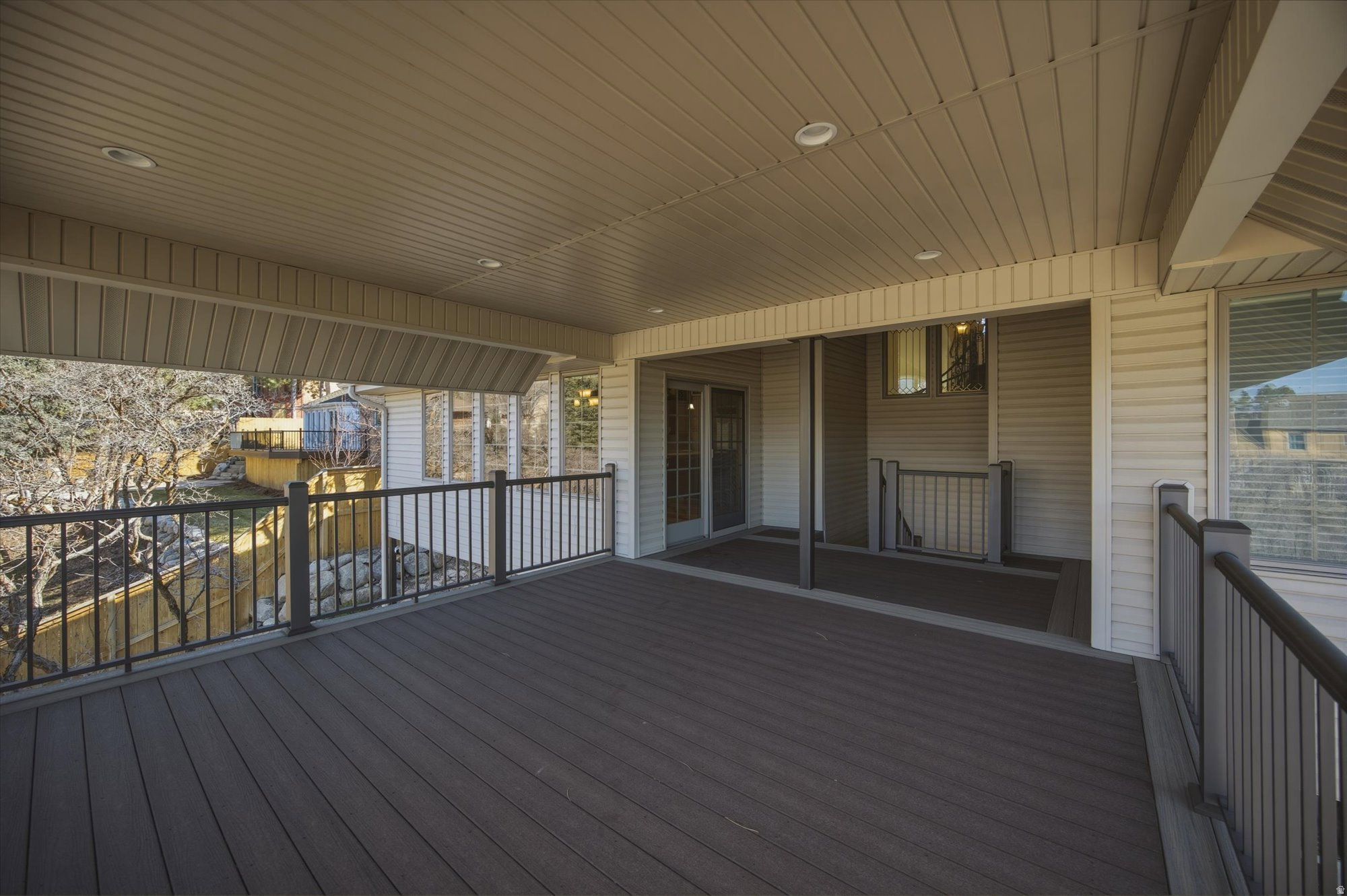 Spacious covered deck featuring composite decking, recessed lighting, and black metal railings