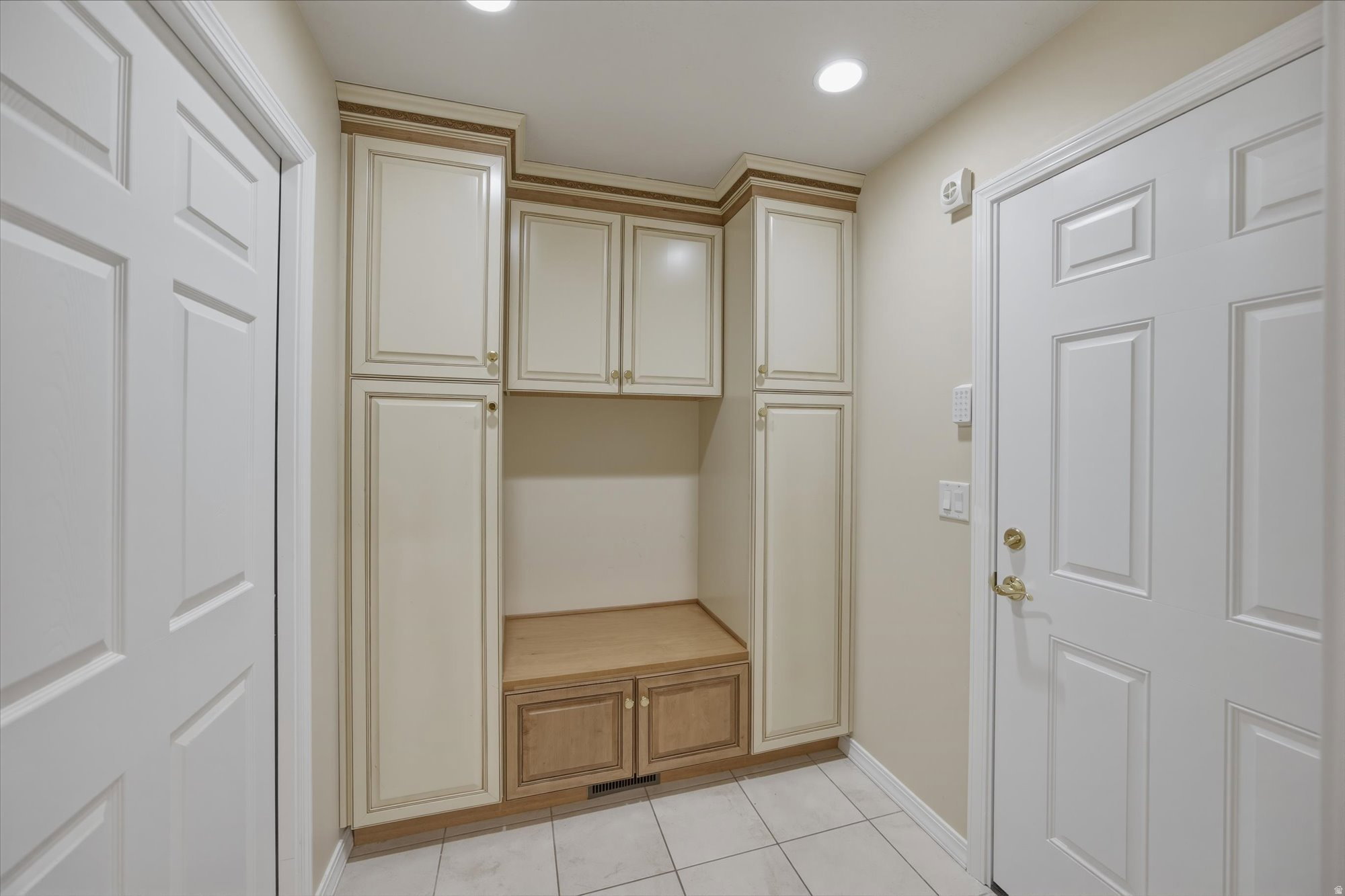 Built-in cabinetry with cream paneling and wood-finish accents, integrated bench seating, recessed lighting, and tile flooring