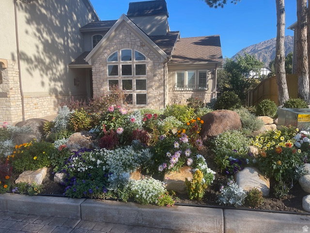 Stone facade residence featuring an arched window, a pitched roofline, and a prominent front garden with diverse plantings and boulders