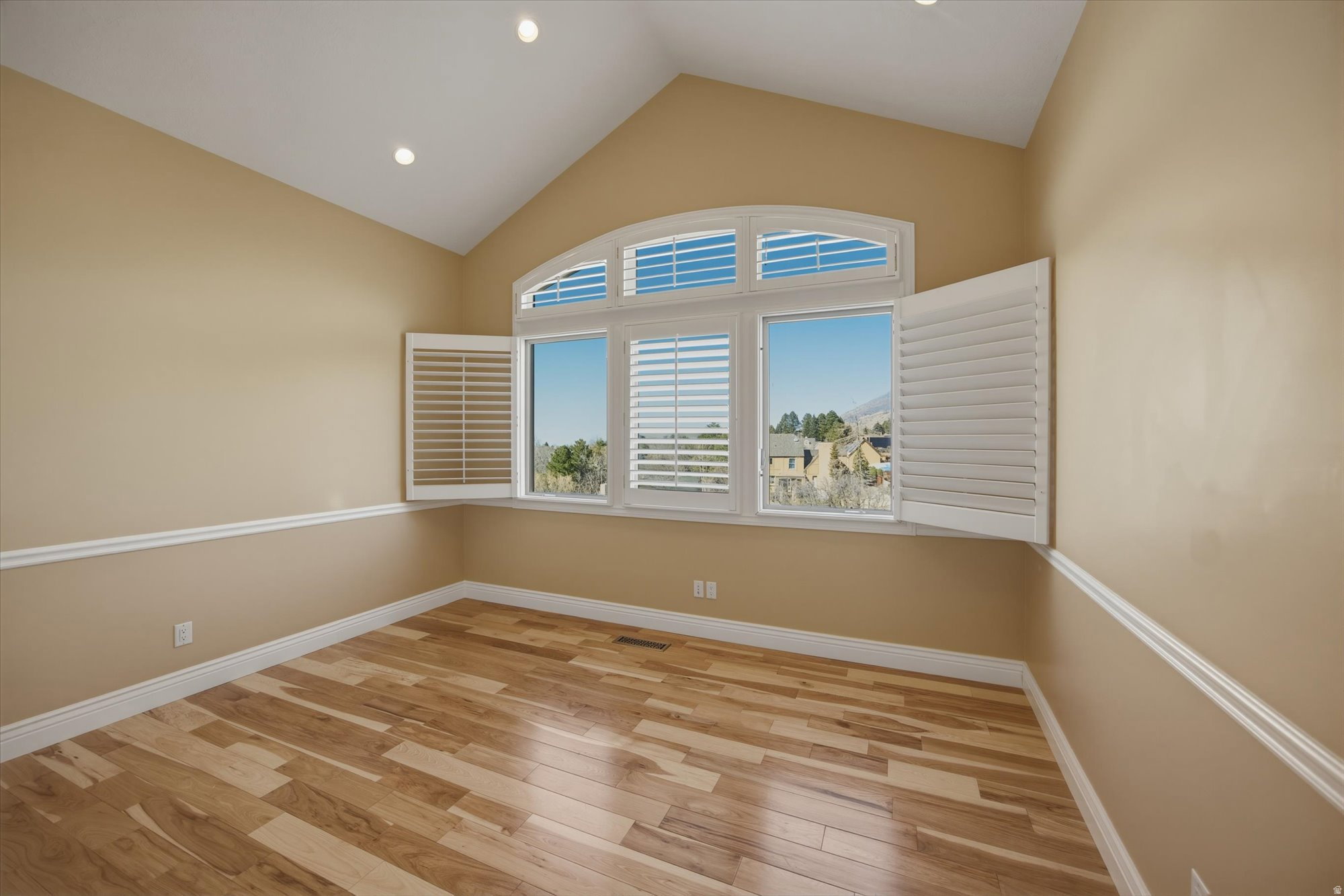 Vaulted ceiling room featuring hardwood flooring and a large arched window with white plantation shutters