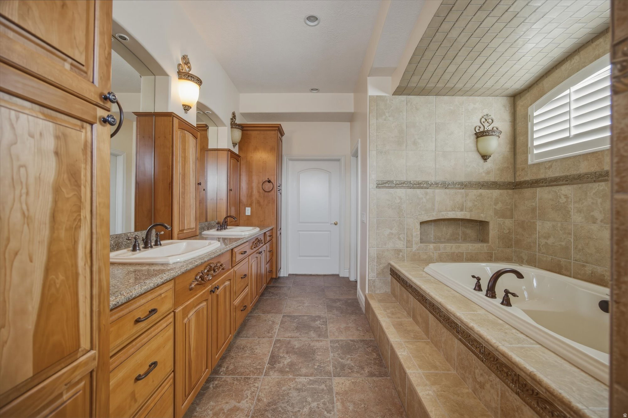 Dual vanity with granite-style countertops, custom wood cabinetry, and integrated sinks