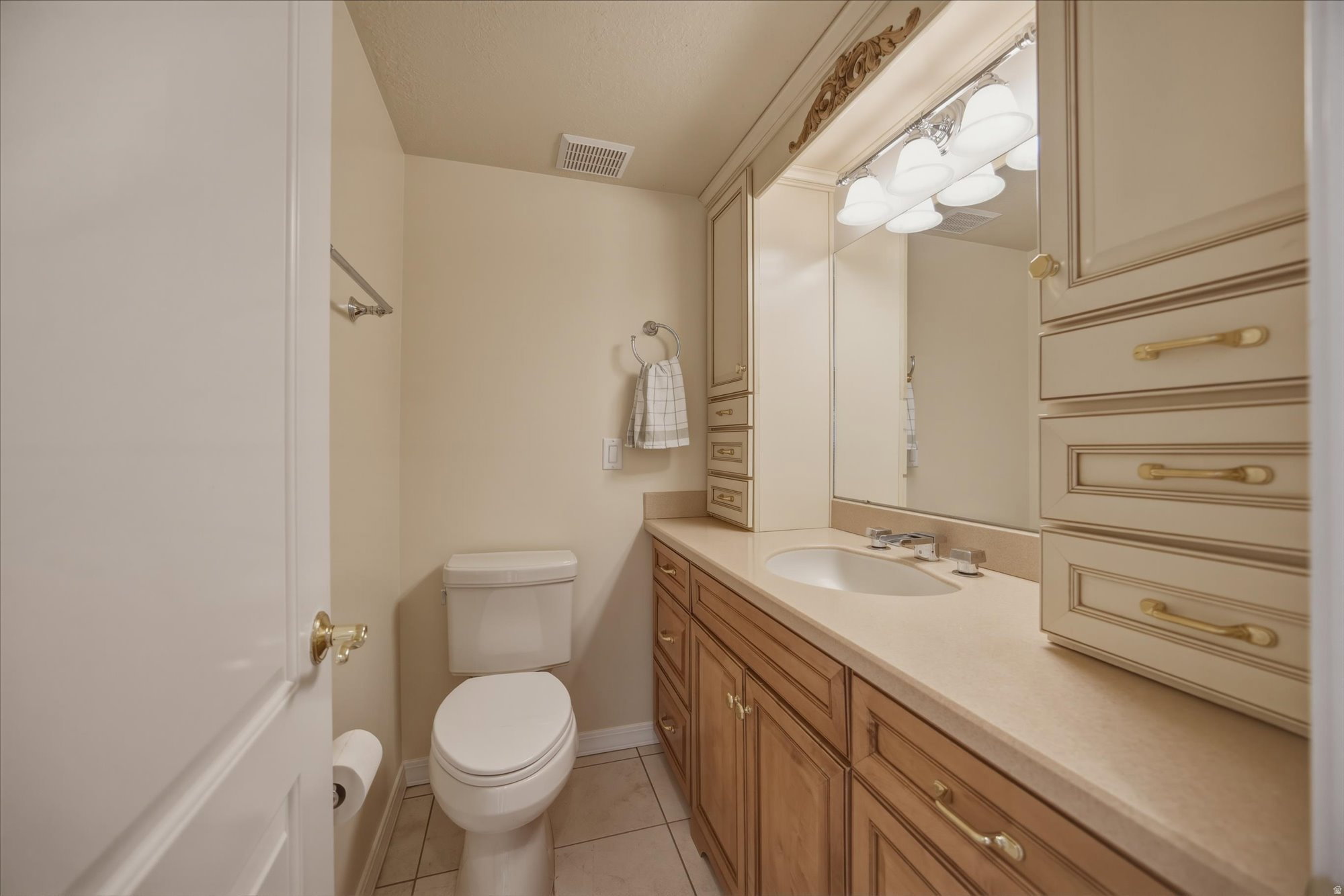 Bathroom featuring a single vanity with an integrated sink, ample storage in both wood-finish and painted cabinetry, a large wall mirror, and overhead vanity lighting