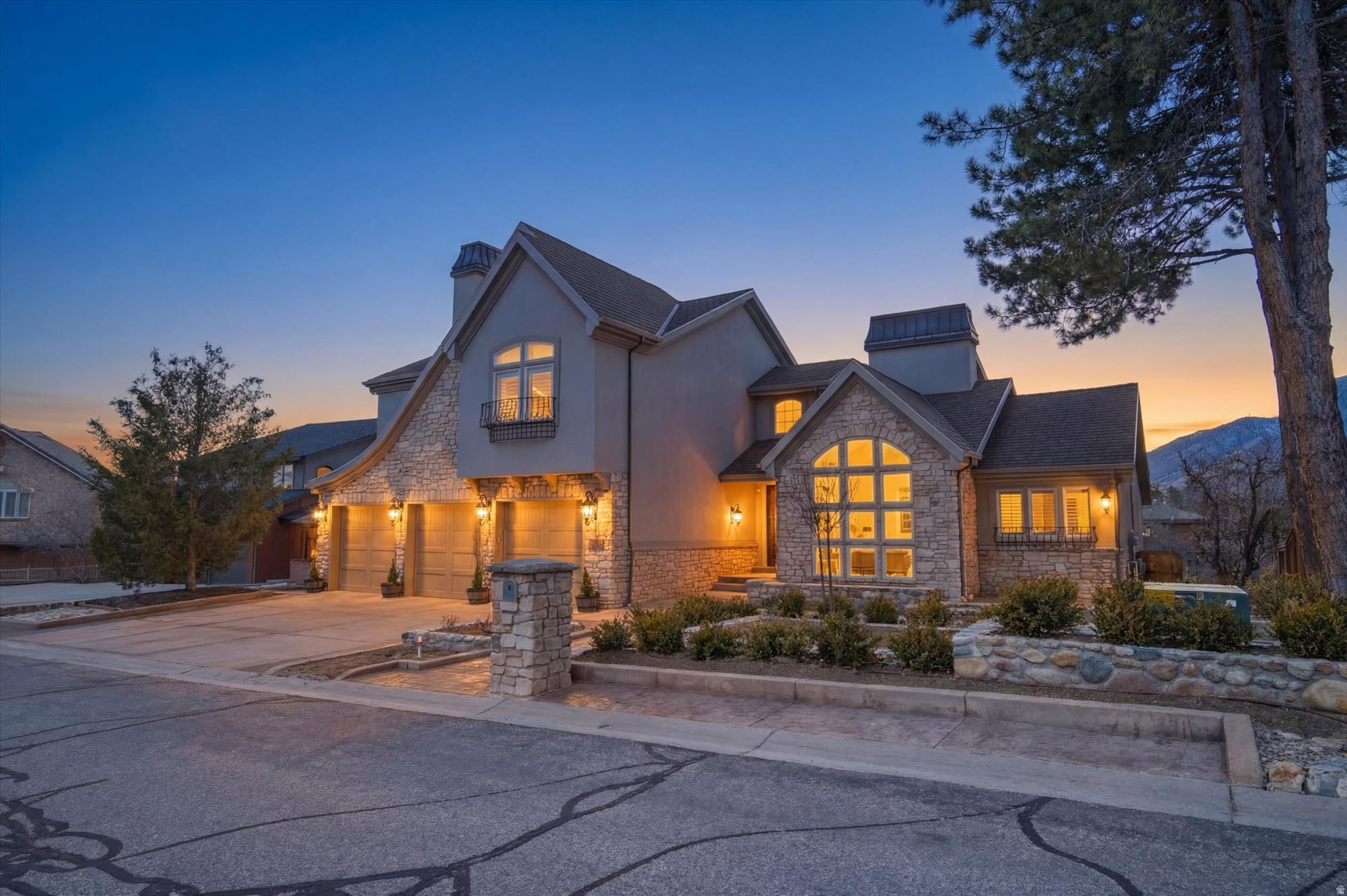 Stucco and stone facade home featuring a prominent arched window, multi-car garage, and established landscaping
