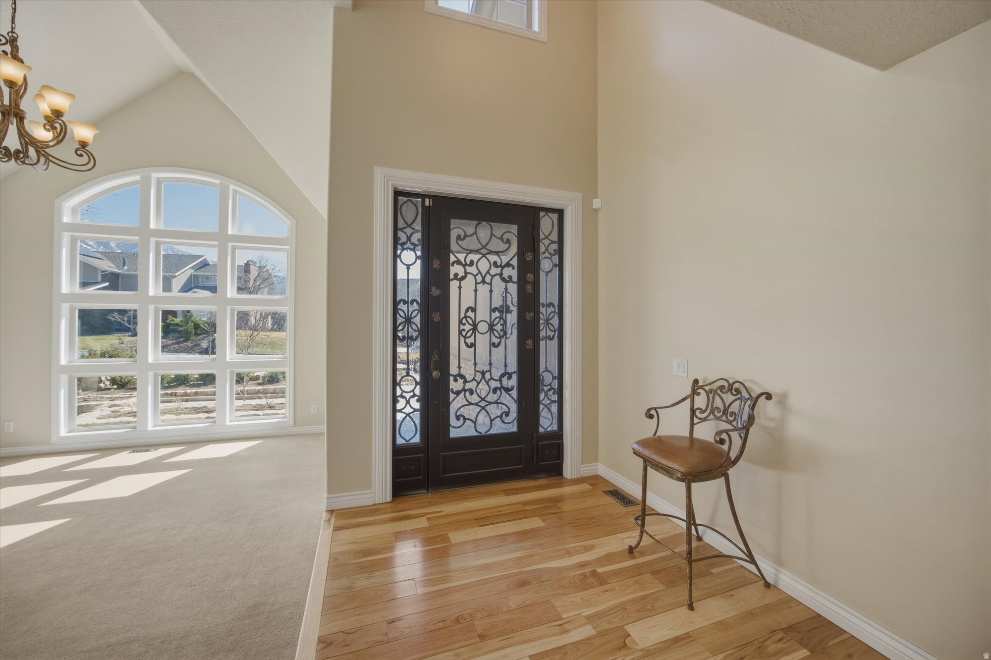 Grand entryway featuring a decorative wrought iron front door, hardwood flooring, and a soaring vaulted ceiling