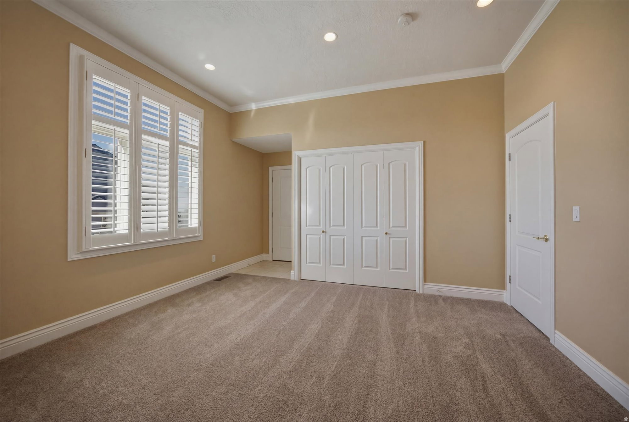 Carpeted room featuring multiple windows with plantation shutters, crown molding, recessed lighting, and a bi-fold closet
