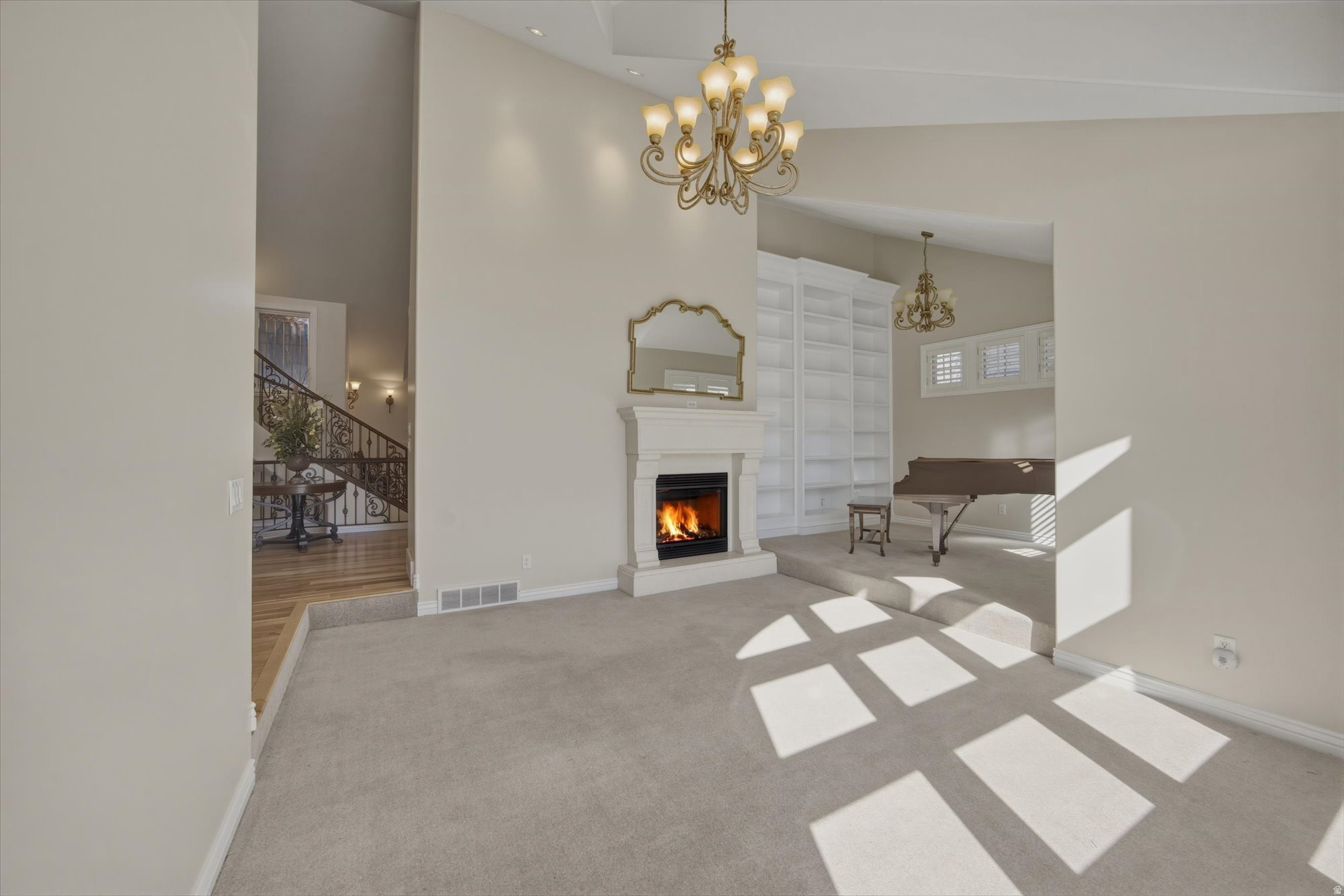 Carpeted living space featuring a white mantel fireplace with a dark insert, a gold-toned chandelier, and a decorative mirror