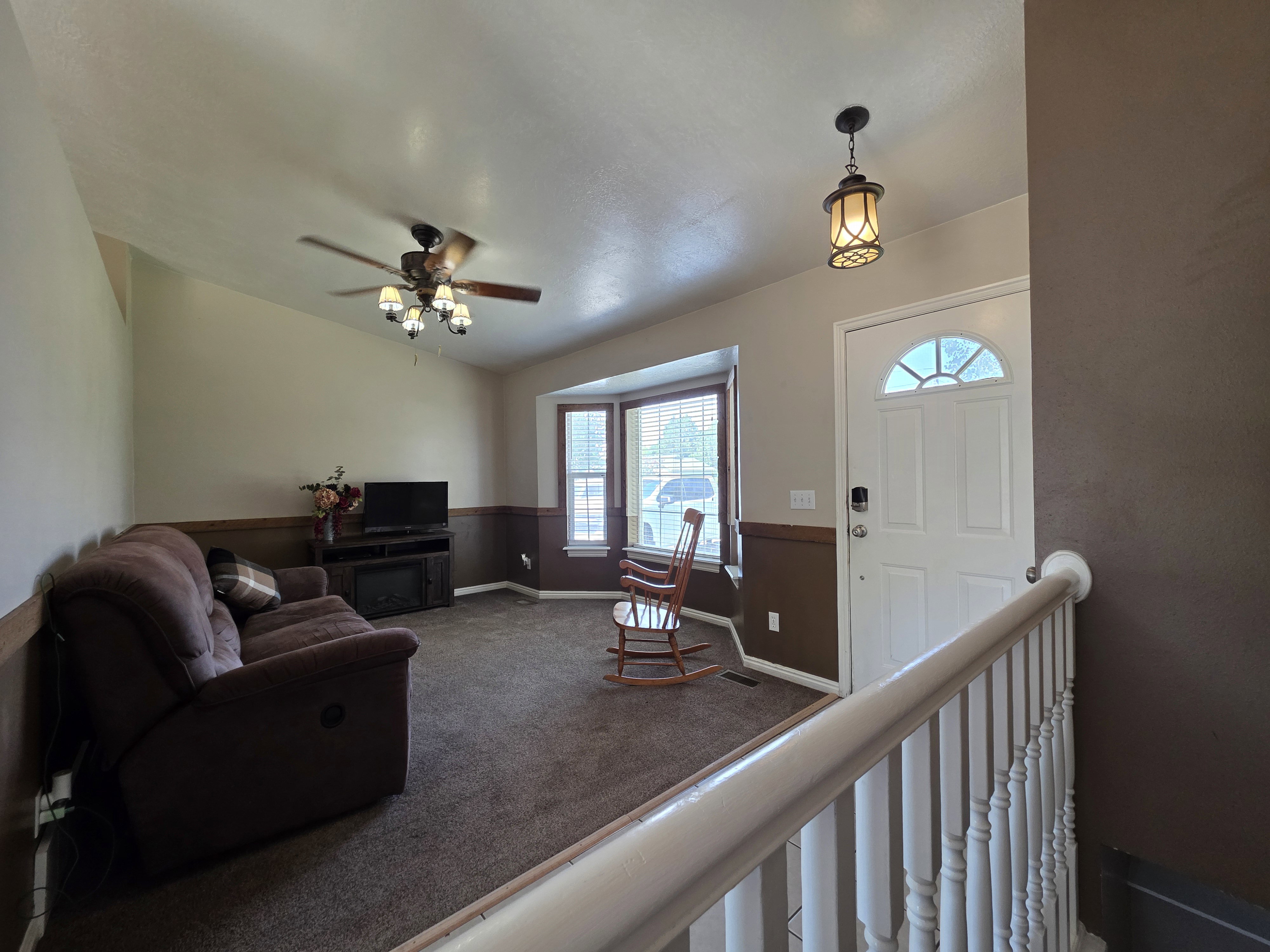 Entryway and living area featuring a white front door with an arched window, a decorative pendant light, and a white baluster railing