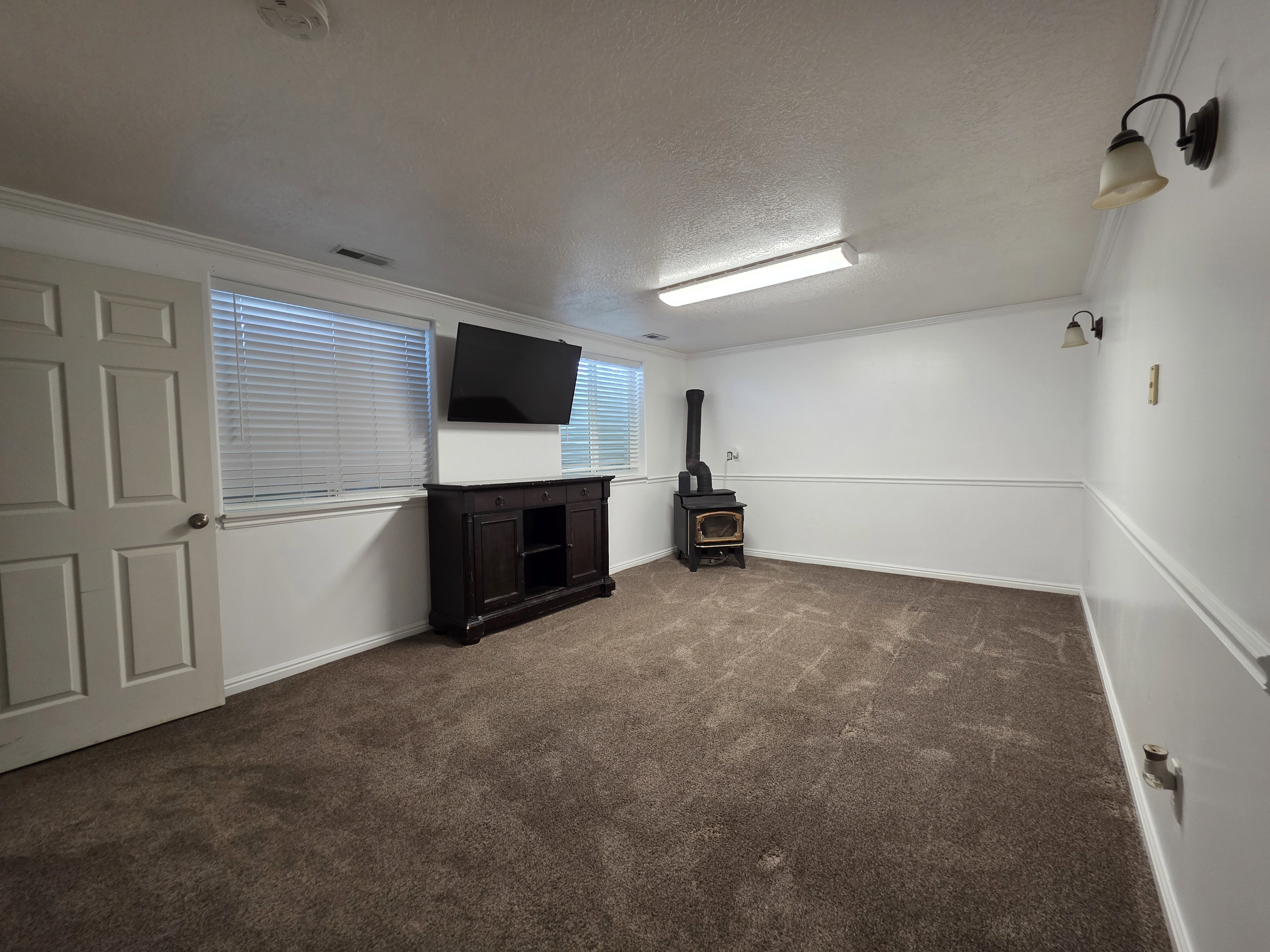 Spacious room featuring broadloom carpet, white walls with wainscoting, and a prominent wood-burning stove