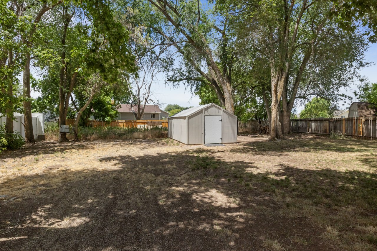Expansive backyard with a freestanding storage shed, mature trees, and a combination of wood and white vinyl fencing