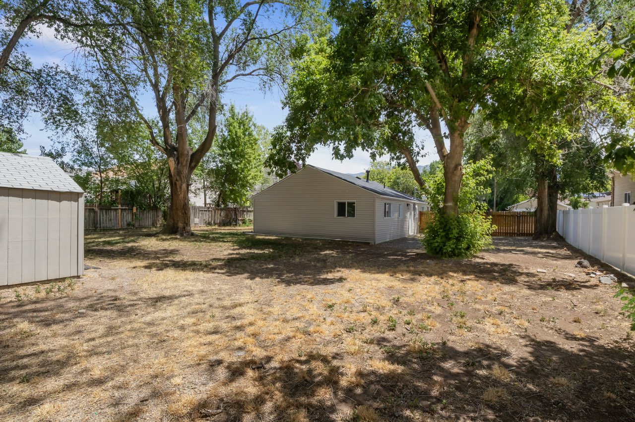 Spacious backyard featuring mature trees, a detached storage shed, privacy fencing, and a separate structure with siding