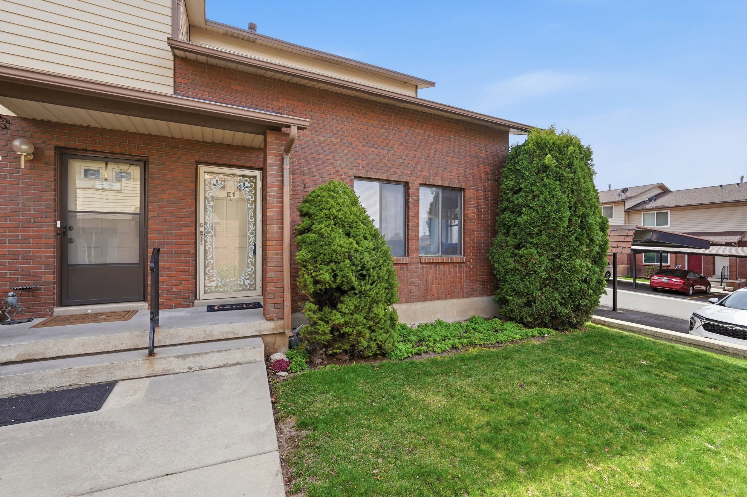Brick exterior featuring a covered entry, established landscaping, and a manicured lawn