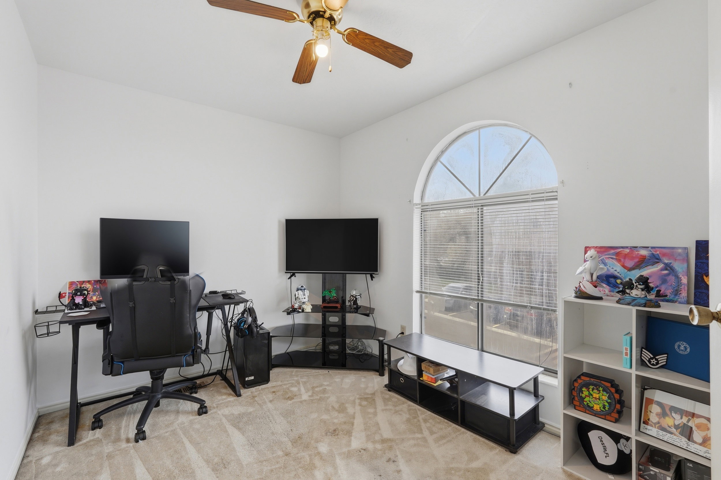 Room featuring a large arched window with horizontal blinds, a ceiling fan with light fixture, and neutral-toned carpeting