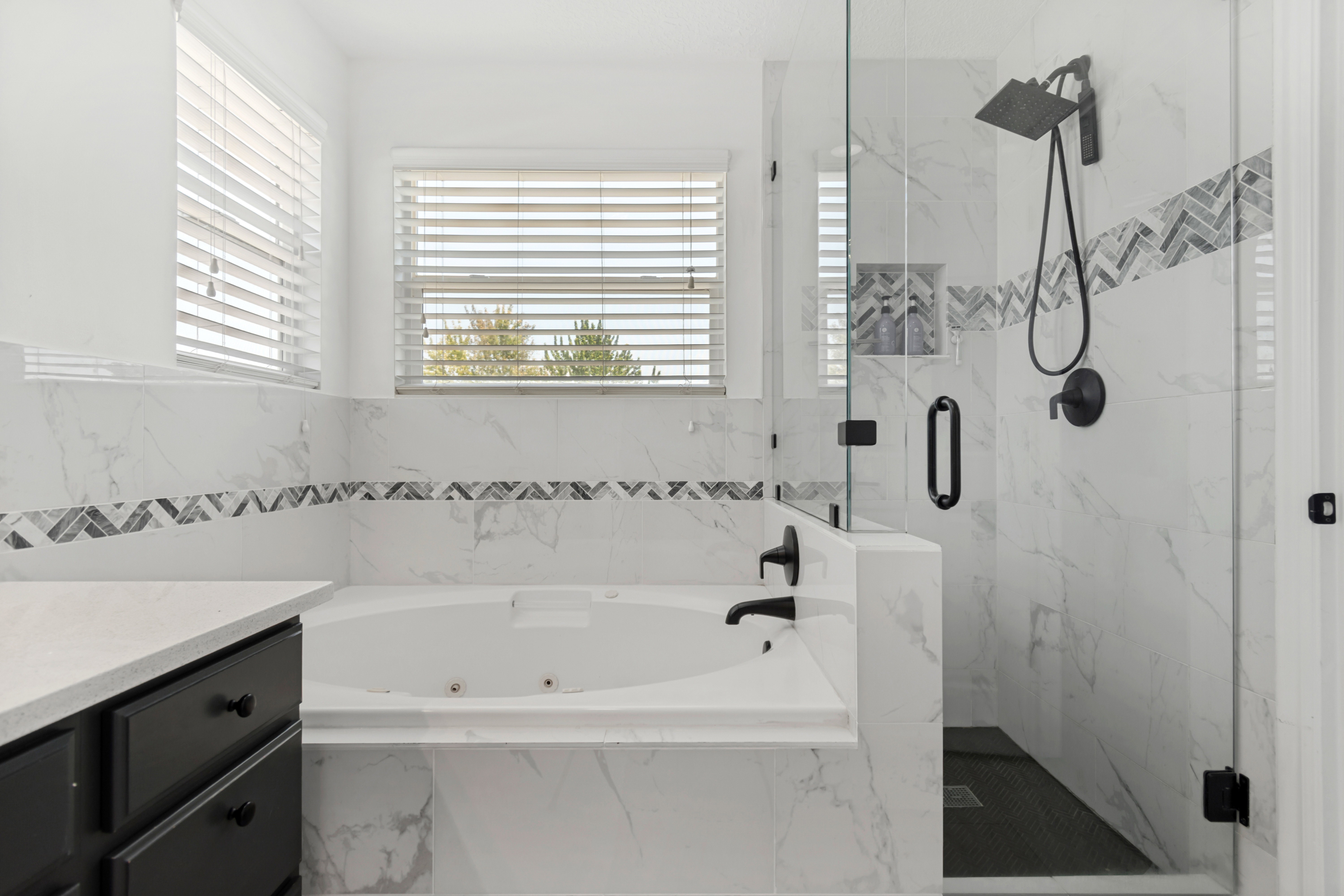 Freestanding tub with white tile surround, glass-enclosed shower with matte black fixtures, and a vanity with a light-colored countertop