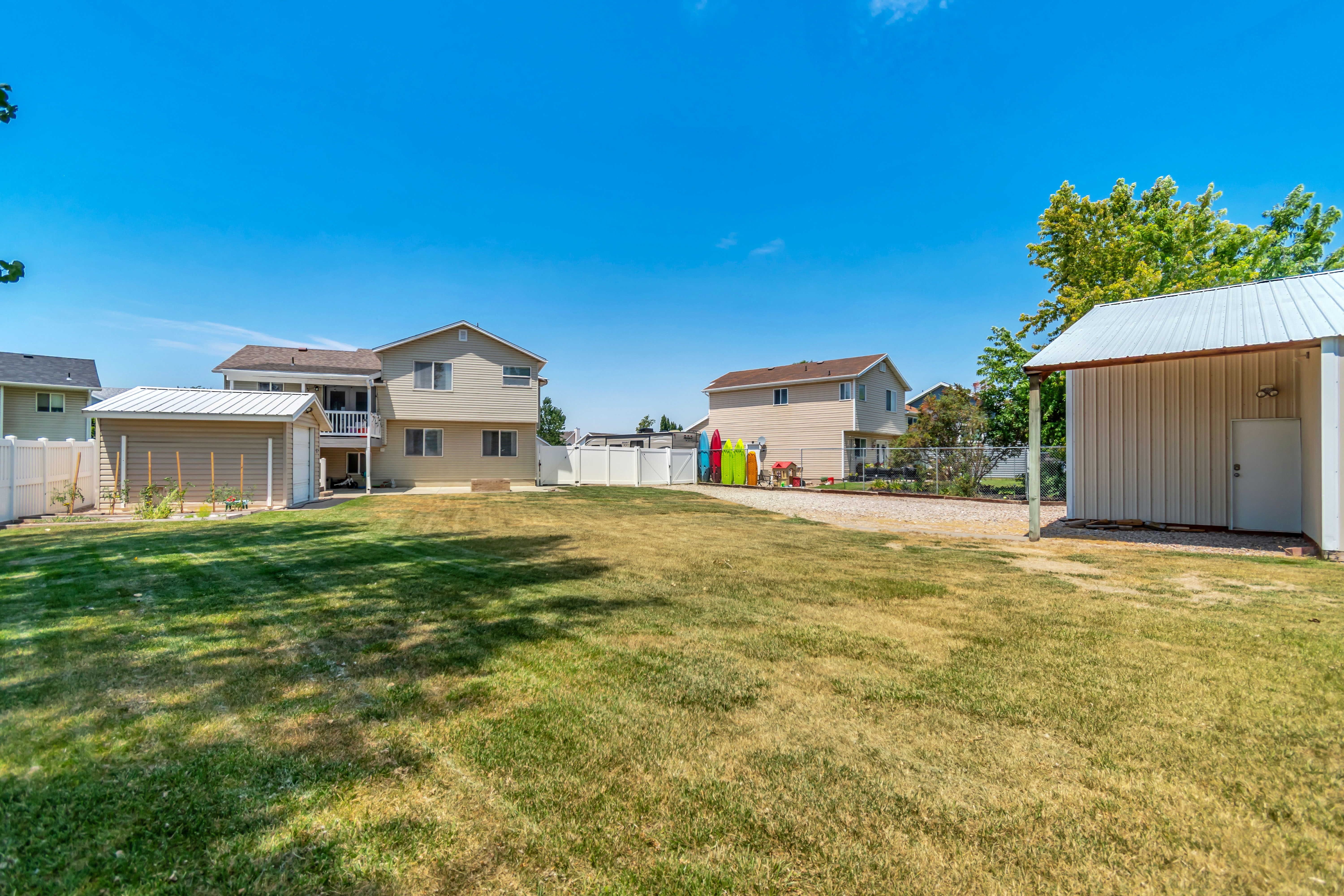 Expansive backyard featuring a large grassy area, a gravel parking area, and two separate storage sheds