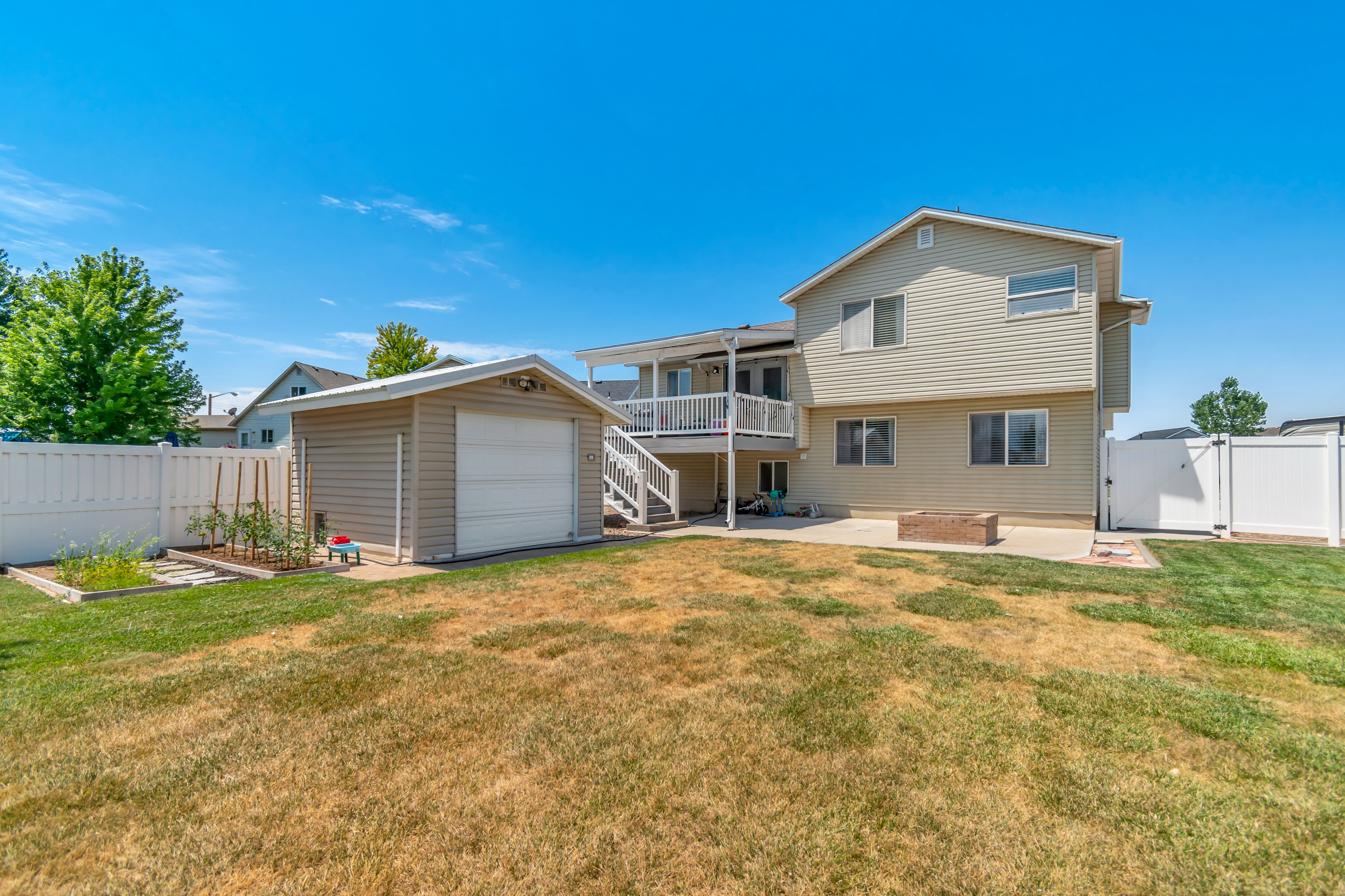 Expansive backyard featuring a detached storage shed, raised garden beds, a concrete patio, and a built-in fire pit