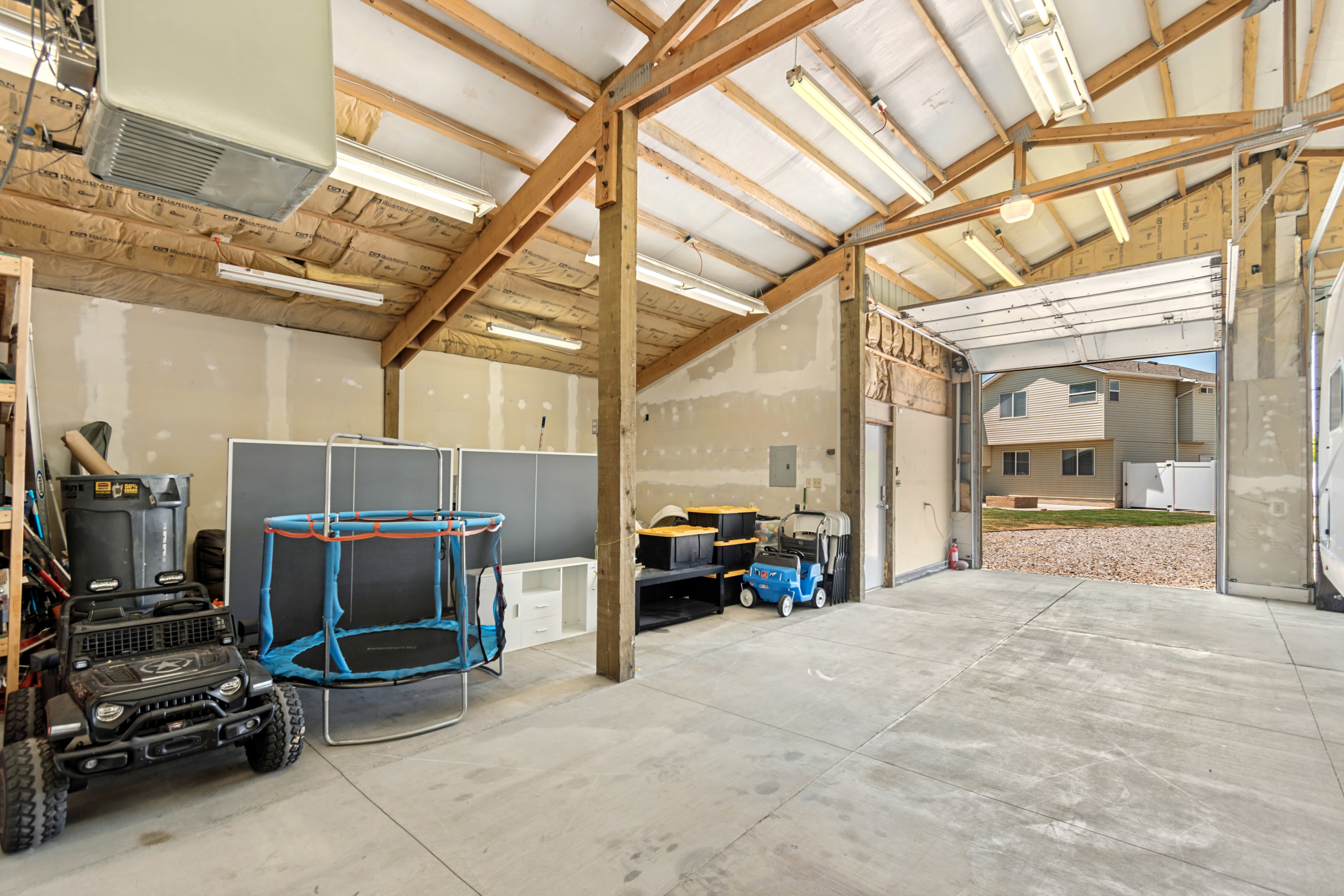 Spacious garage with exposed wood beam ceiling, concrete flooring, fluorescent lighting, and a large roll-up door