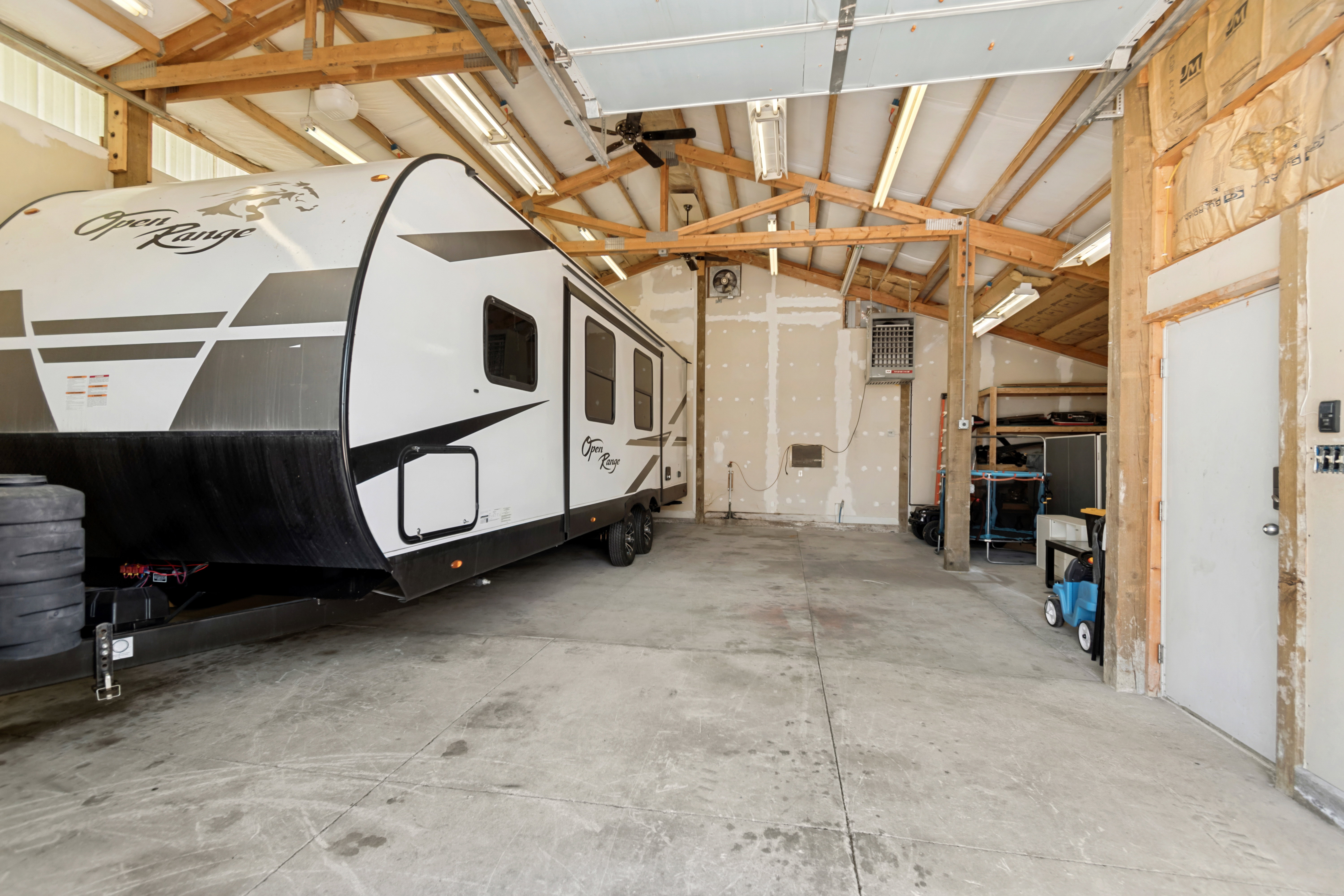 Spacious garage featuring a concrete floor, exposed wood trusses, ceiling-mounted fluorescent lighting, and a roll-up garage door
