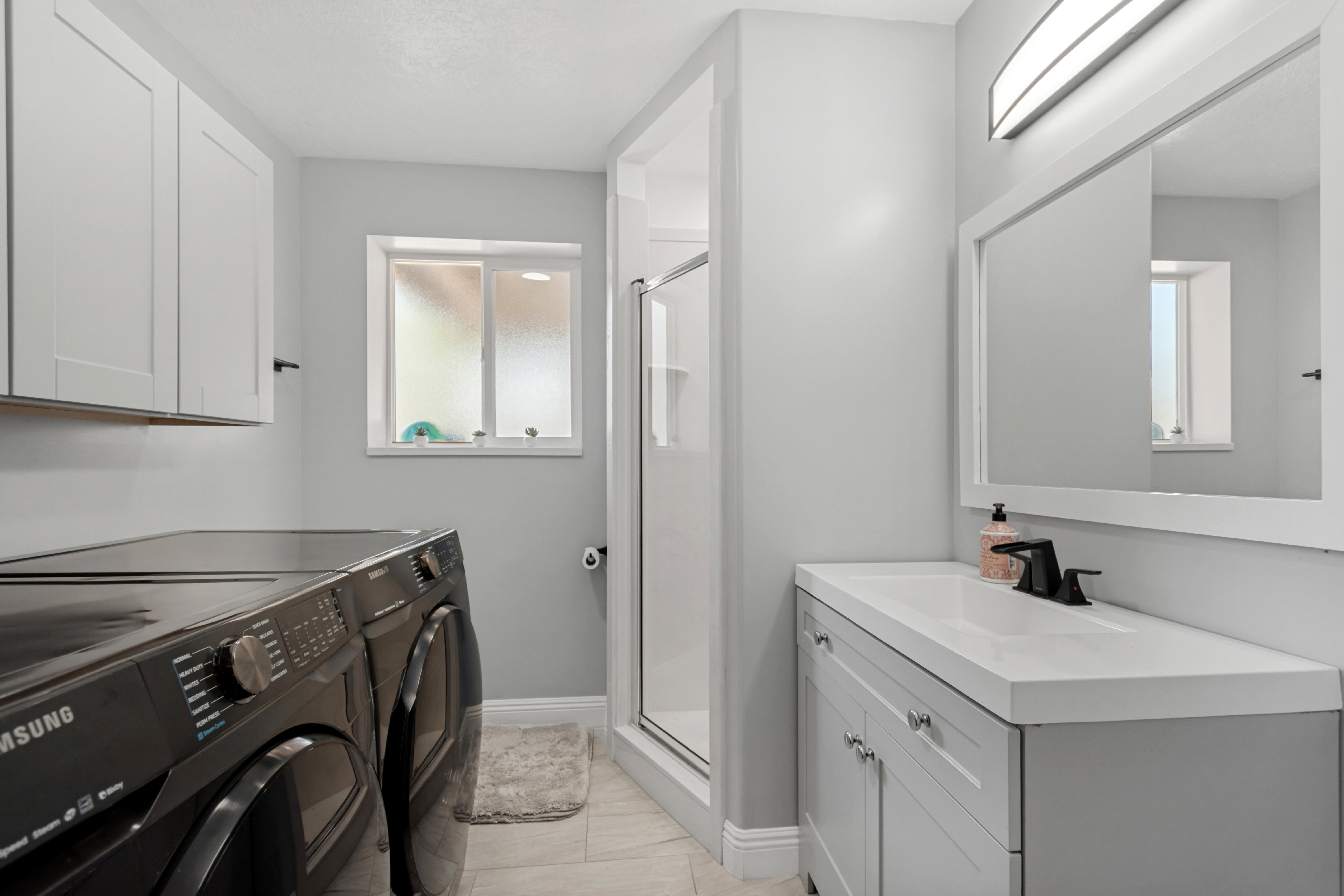 Bathroom featuring a single vanity with a white countertop, matte black faucet, and a framed mirror with integrated lighting