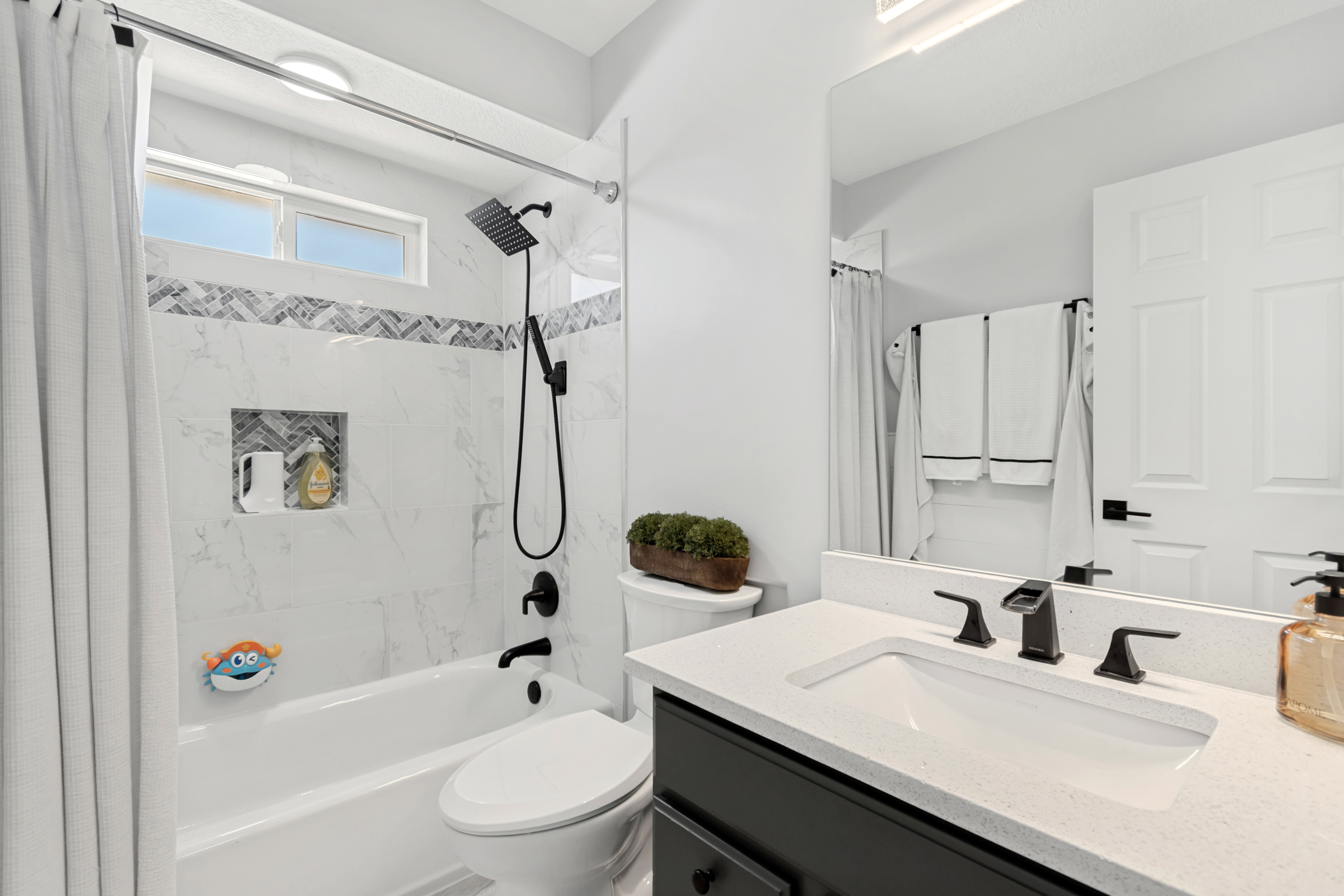 Bathroom featuring a white bathtub with a built-in shower niche and decorative tile band, a vanity with a white countertop and rectangular undermount sink, and matte black plumbing fixtures