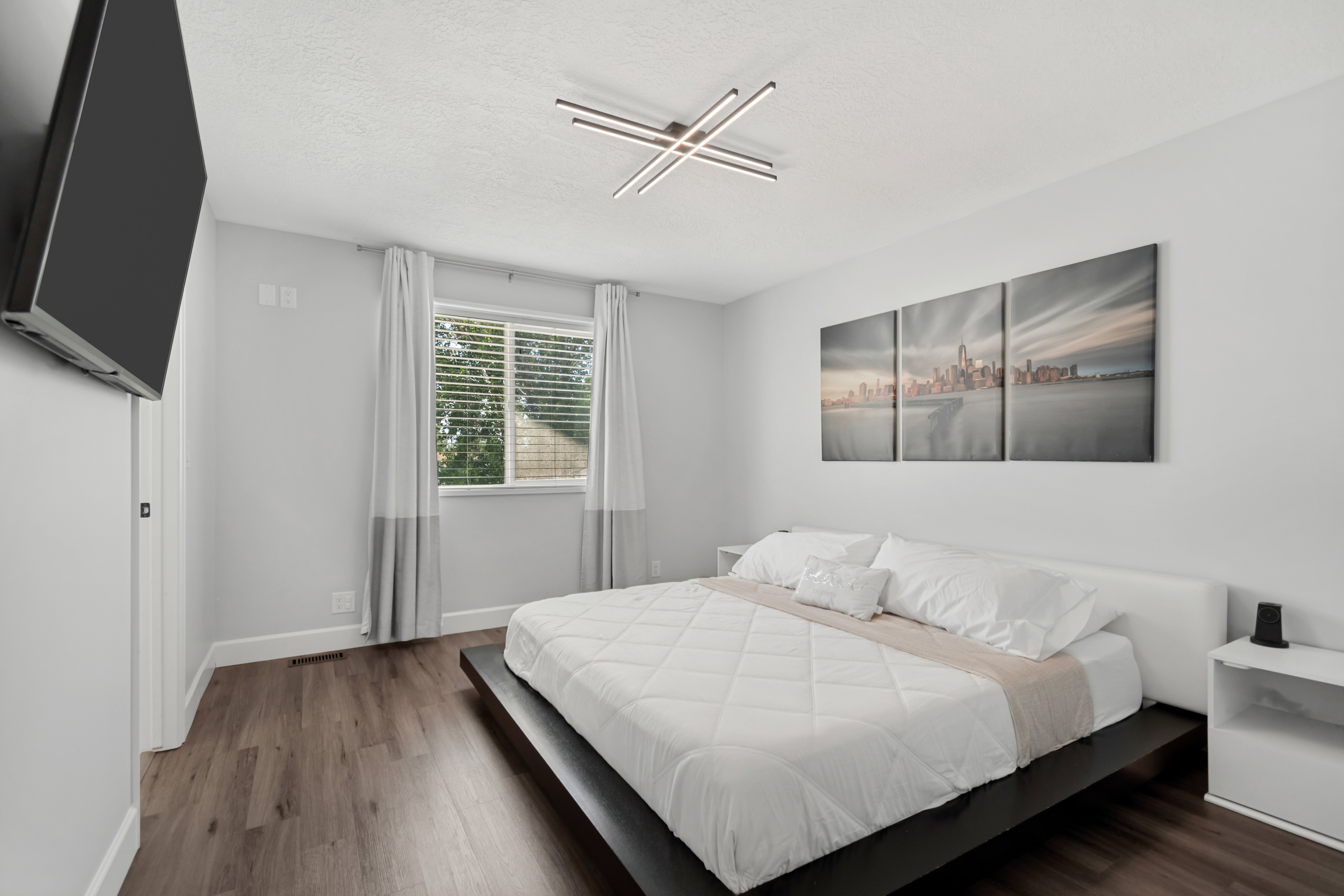 Bedroom featuring wood-finish flooring, a window with blinds, a sleek ceiling light fixture, and white wall finishes