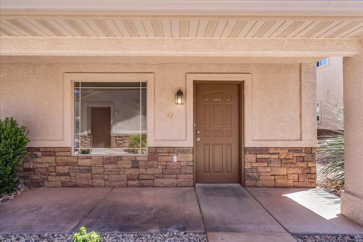 A welcoming, covered entry creates a warm first impression, highlighted by a stucco exterior with stacked stone accents, a paneled front door, and charming grid-style windows.