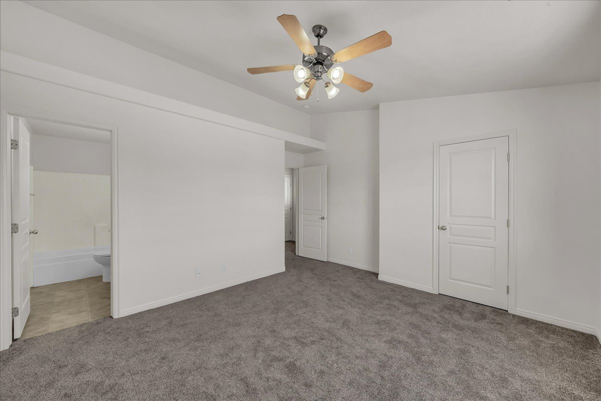 Spacious primary suite featuring soft neutral finishes, plush carpeting, a ceiling fan, and convenient access to the walk-in closet and en-suite bath.