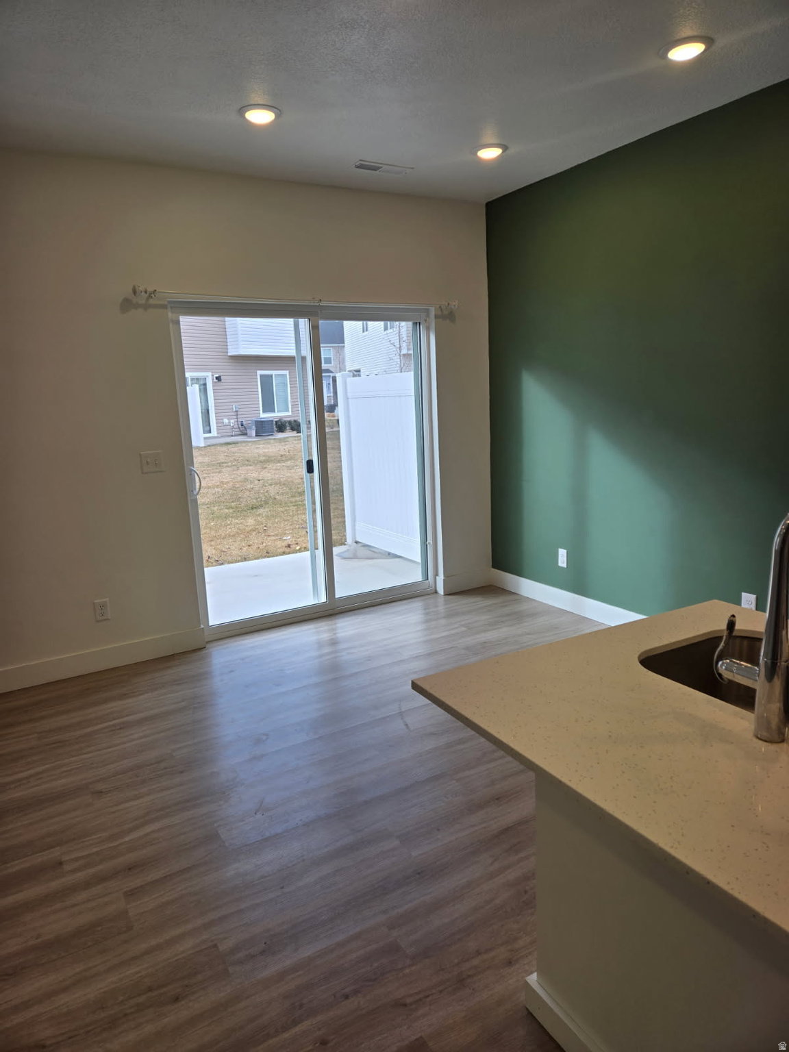 Expansive living area featuring wood-finish flooring, recessed lighting, and a sliding glass door providing access to the backyard