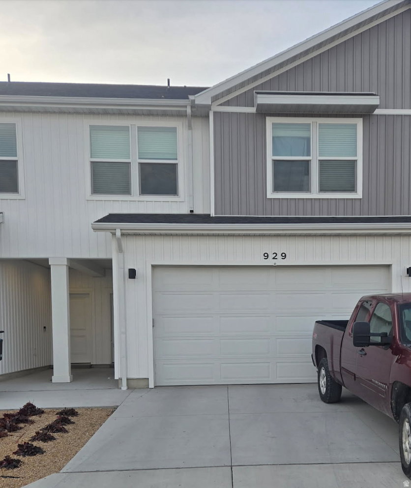 Contemporary townhome exterior featuring a two-car garage, vertical and horizontal panel siding, a covered entry, and a paved driveway