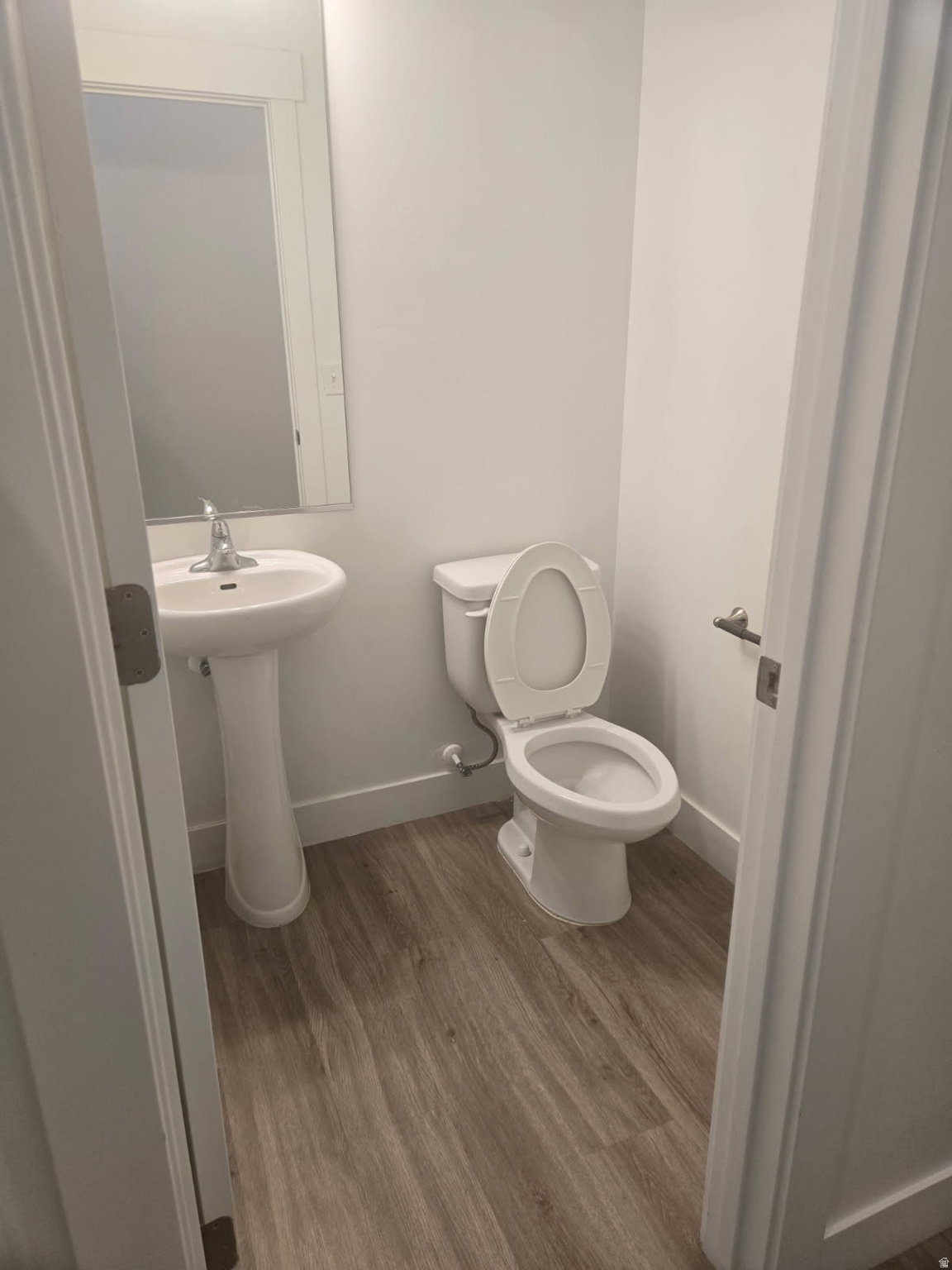 Powder room featuring a pedestal sink, wall-mounted mirror, and wood-finish flooring