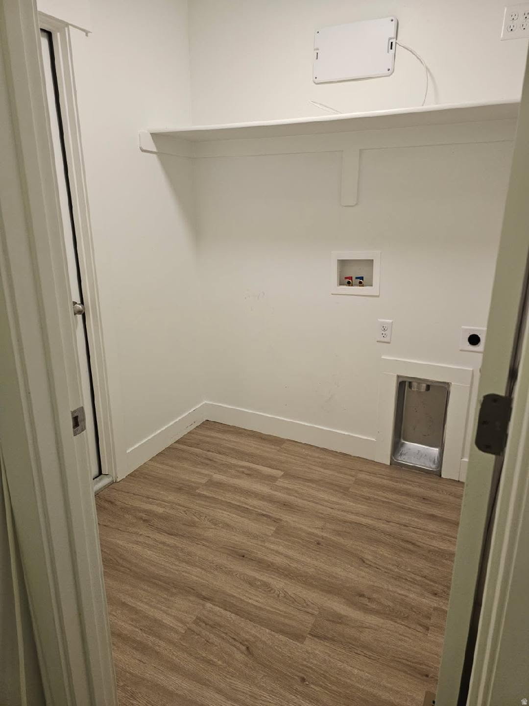 Dedicated utility room featuring wood-finish flooring, crisp white walls, and a built-in storage shelf