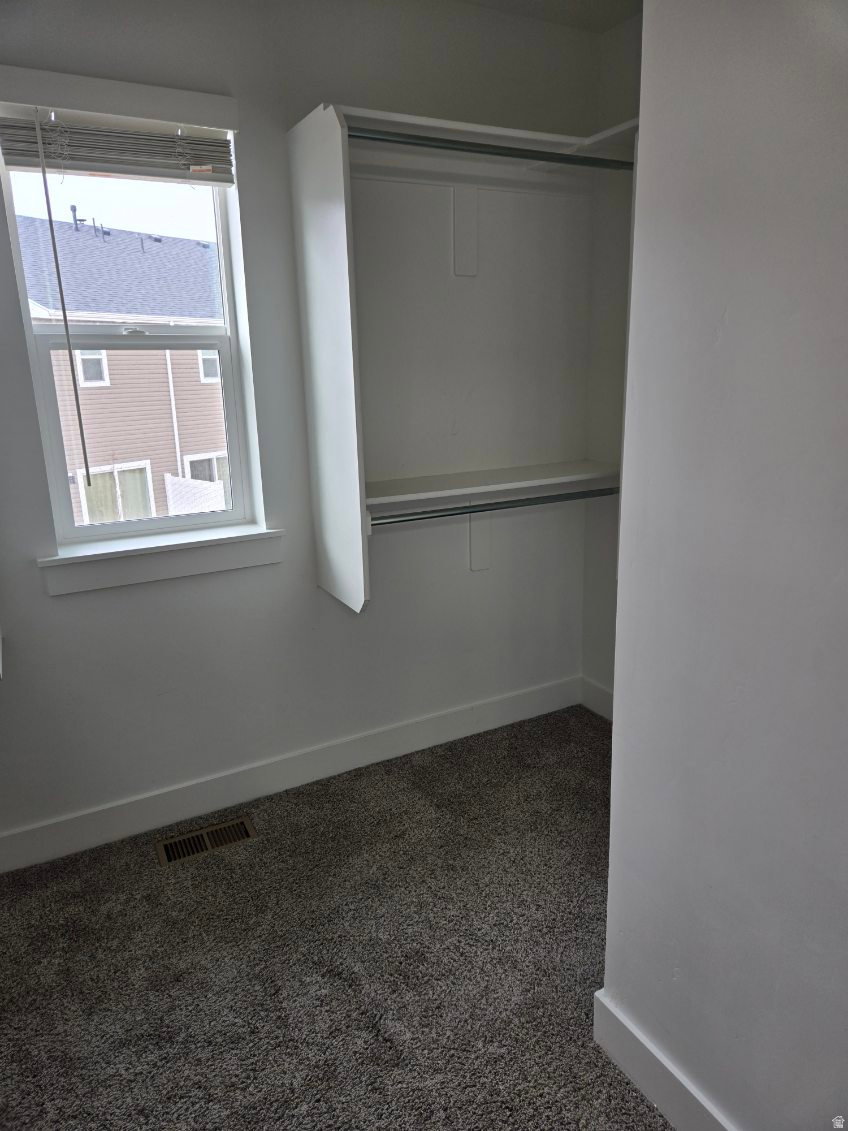 Bedroom space featuring a double-hung window, built-in closet organization with shelving and hanging rods, neutral wall paint, and gray textured carpeting
